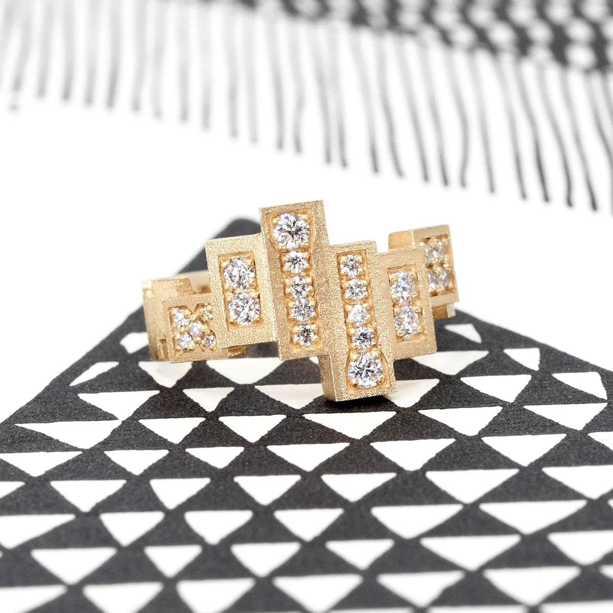 Unique, highly original ring in yellow gold with a rough finish made of several gold rectangles assembled side by side in a staggered fashion. Several of these blocks are set with extra-brilliant diamonds. The result is a jewel with a futuristic, geometric look. This fine piece of jewelry was designed and created in Montreal, Canada, by independent brand Bena Jewelry. The jewel is photographed from the side in an artistic black and white image.