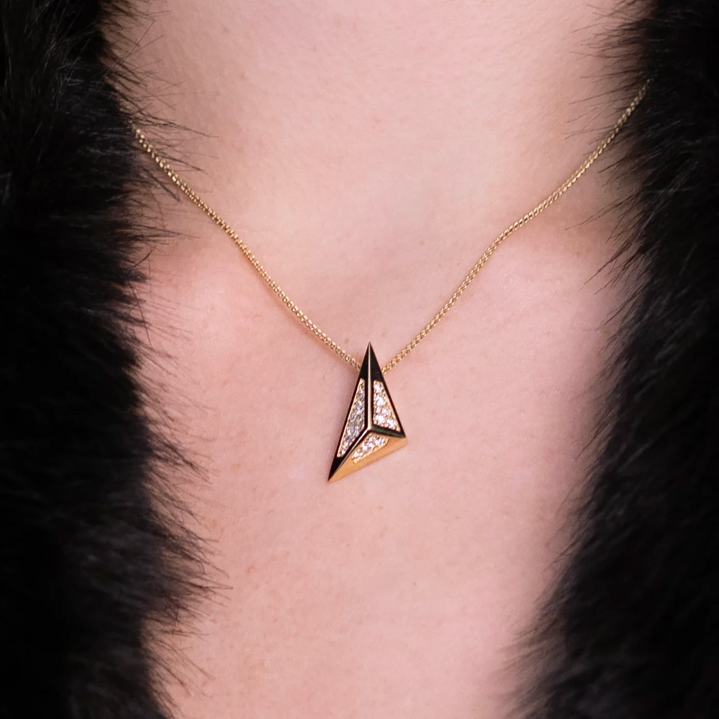 Close-up of an architectural pendant in 14k yellow gold with black enamel and pavé-set diamonds, featuring a bold triangular design. A sculptural statement necklace by Bena Jewelry, handcrafted in Montreal.