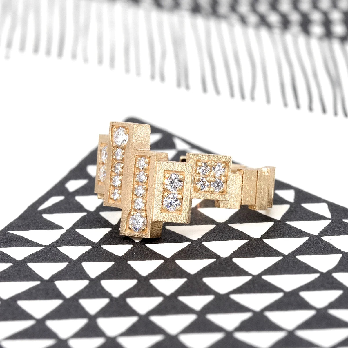Unique, highly original ring in yellow gold with a rough finish made of several gold rectangles assembled side by side in a staggered fashion. Several of these blocks are set with extra-brilliant diamonds. The result is a jewel with a futuristic, geometric look. This fine piece of jewelry was designed and created in Montreal, Canada, by independent brand Bena Jewelry. The jewel is photographed from the side in an artistic black and white image.