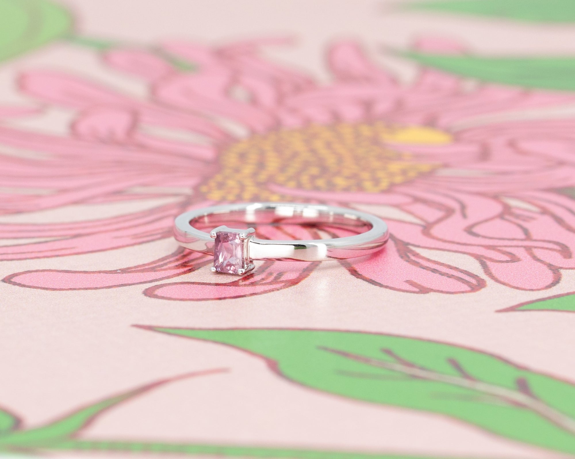 Modern white gold ring featuring a baguette-cut pink sapphire, styled on a rose-toned backdrop. Handmade by Bena Jewelry.