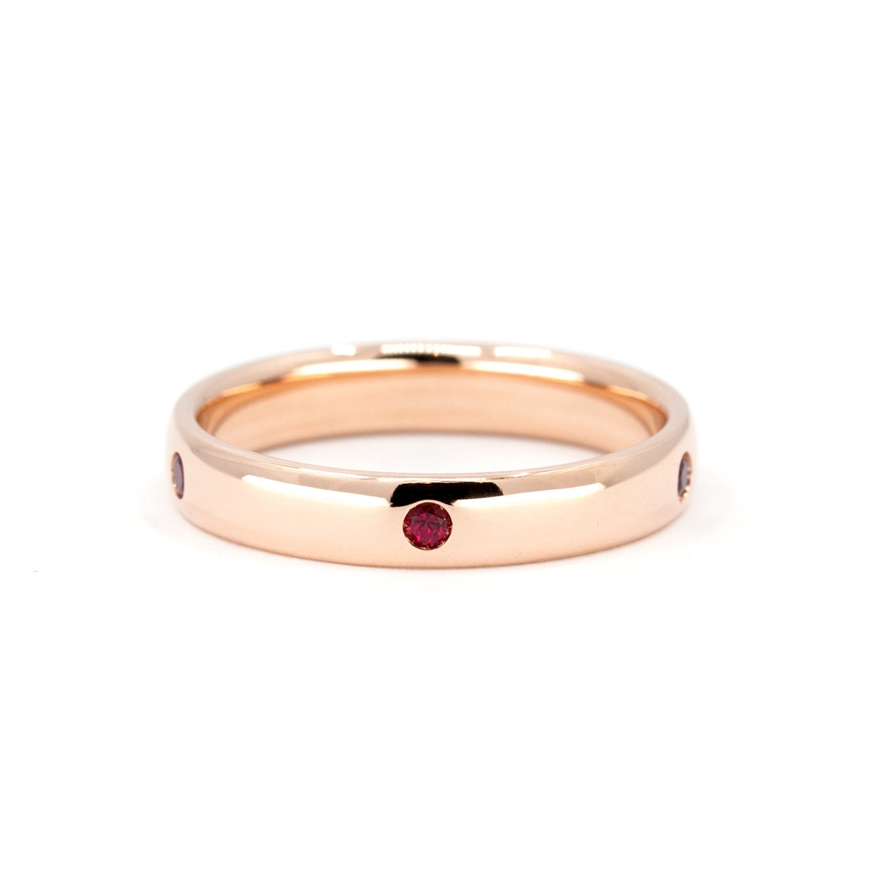 Men&#39;s rose gold wedding band with bezel-set pigeon blood rubies and a subtle dome, crafted by Bena Jewelry in Montreal, Canada.