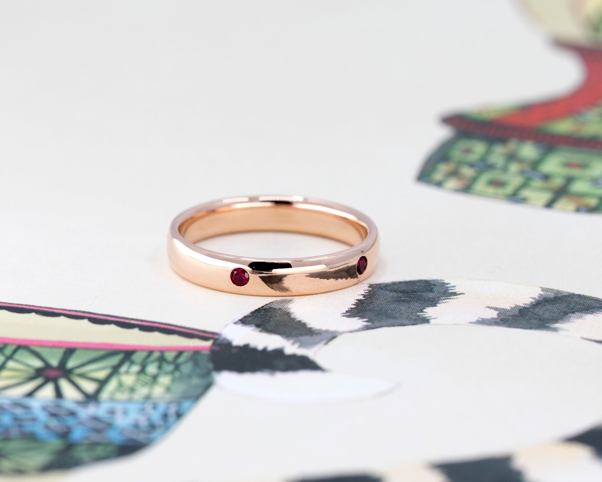 Elegant men’s rose gold wedding band with pigeon blood rubies, displayed on a soft-toned background. Designed by Bena Jewelry in Montreal.