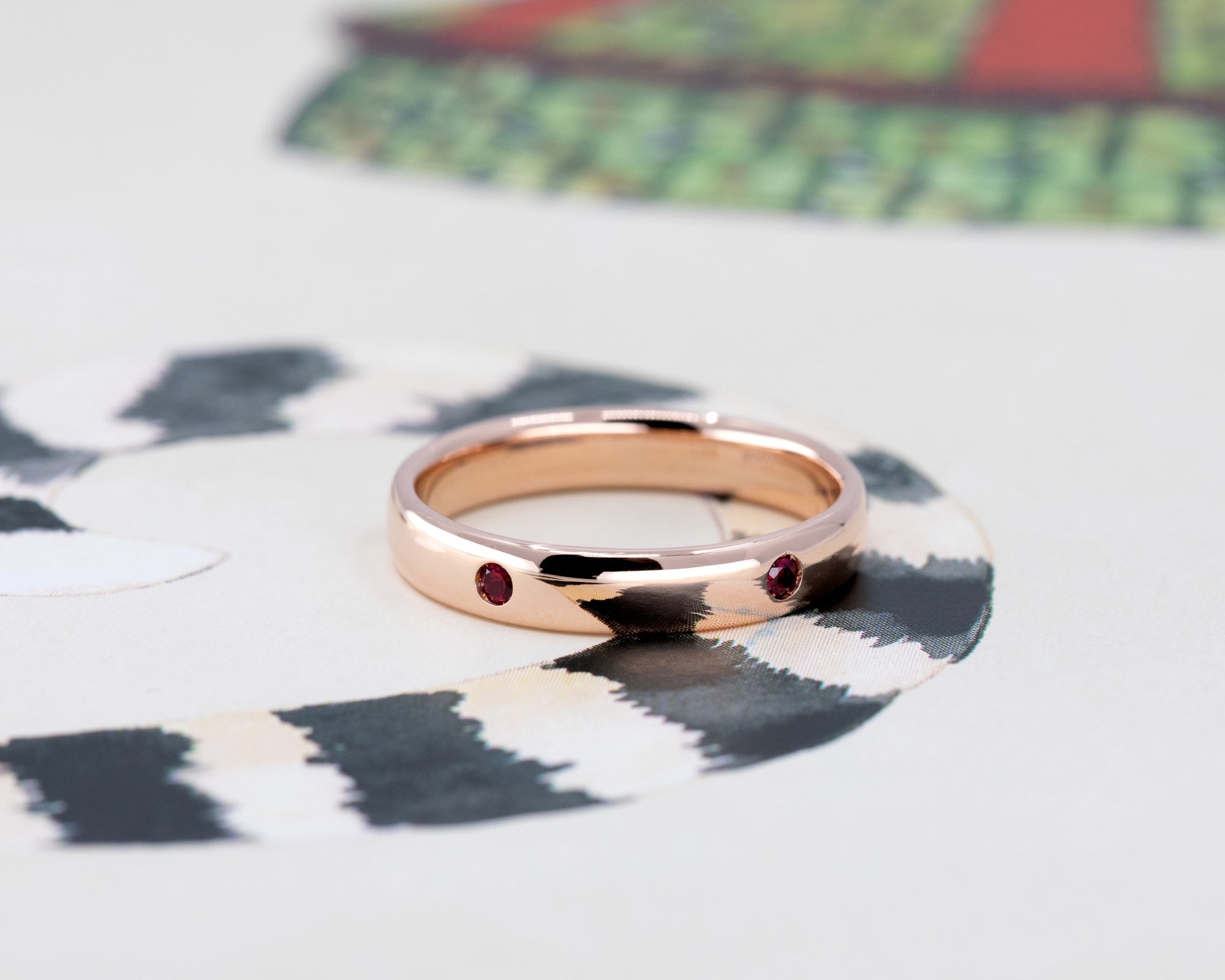 Rose gold ring with bezel-set rubies, styled on a light background. Handmade by Bena Jewelry, a Canadian jewelry designer.