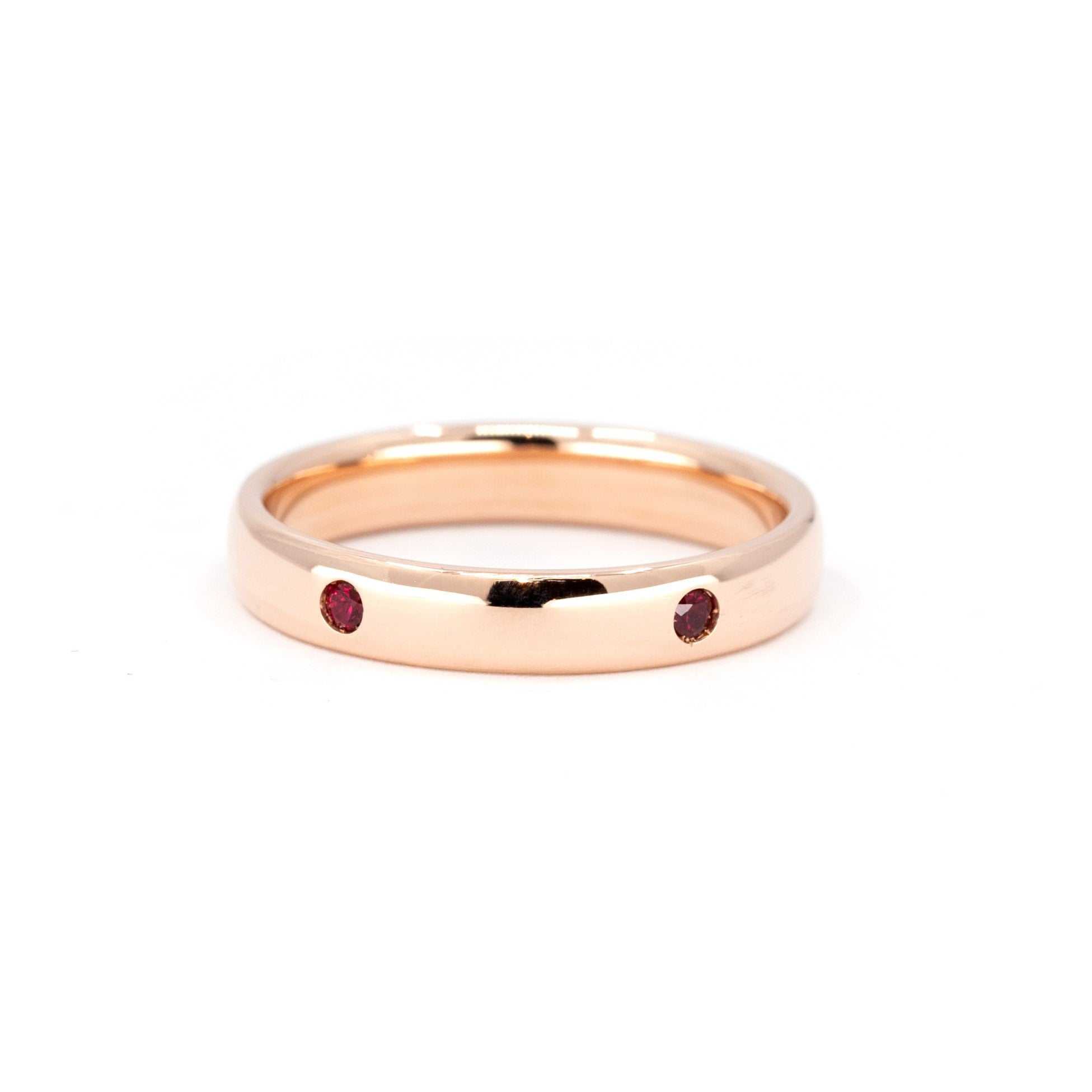 Custom men’s rose gold wedding band with round rubies, set against a soft-colored background. Designed by Bena Jewelry in Montreal.