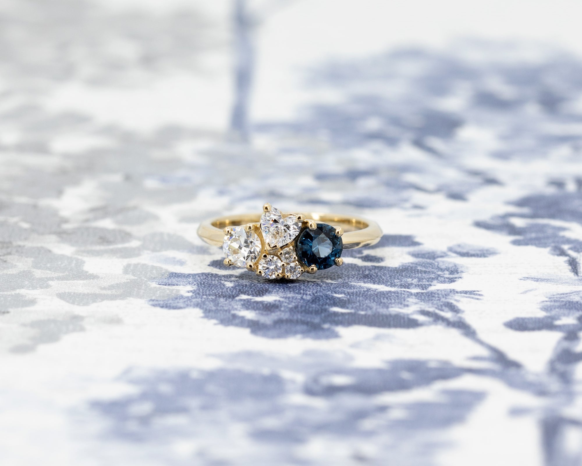 Yellow gold ring with blue spinel and diamonds, displayed on a soft blue background, crafted by Bena Jewelry in Montreal.