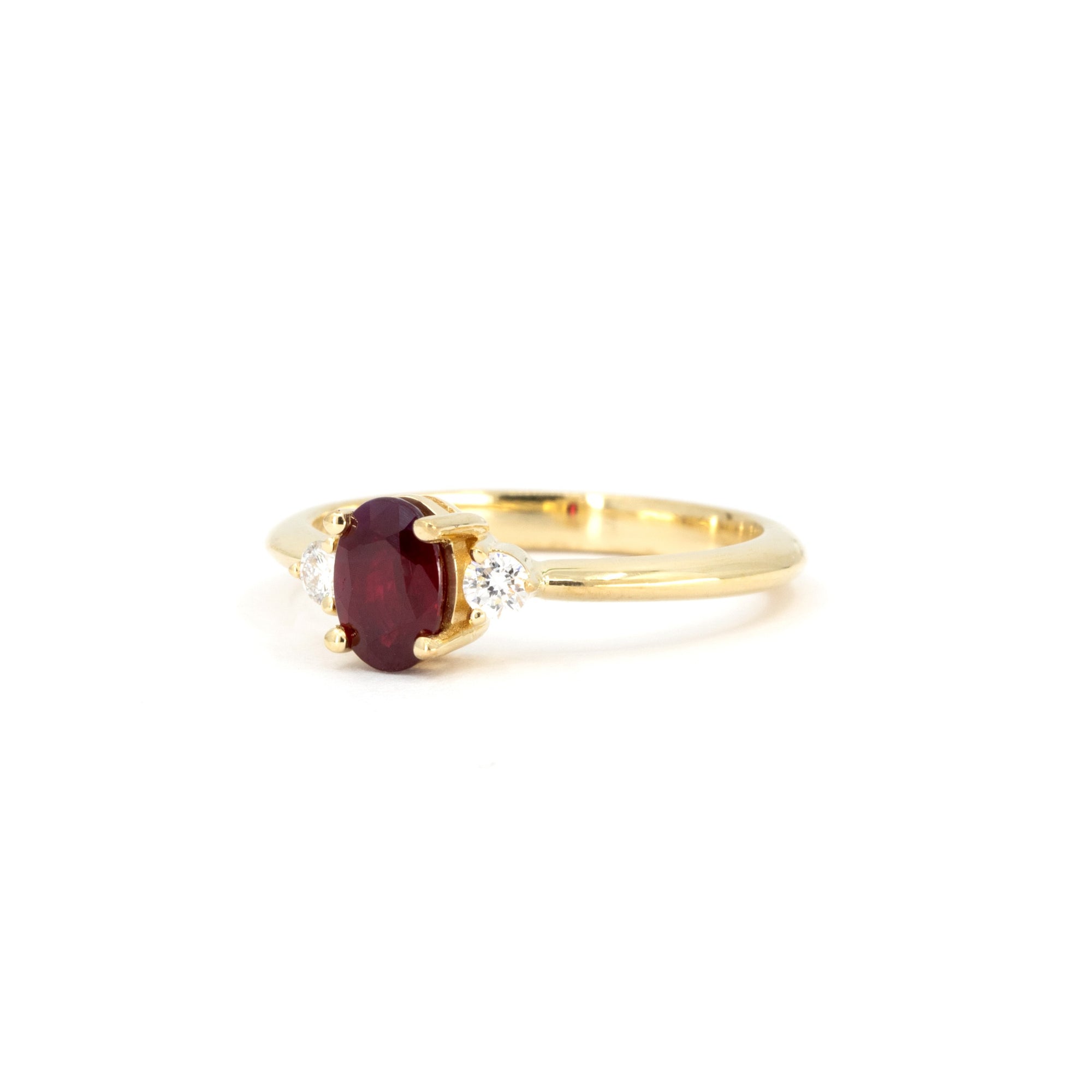 Side view of ruby engagement ring – A warm yellow gold band elegantly holding an oval ruby and two brilliant diamonds.