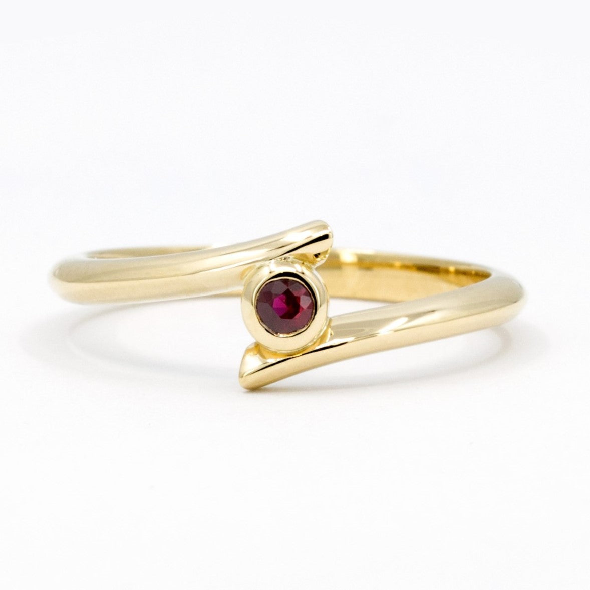 Kink Ruby ring with a blood-red round ruby in a bezel setting, mounted on yellow gold. Edgy twisted band design, handcrafted by Bena Jewelry in Montreal.