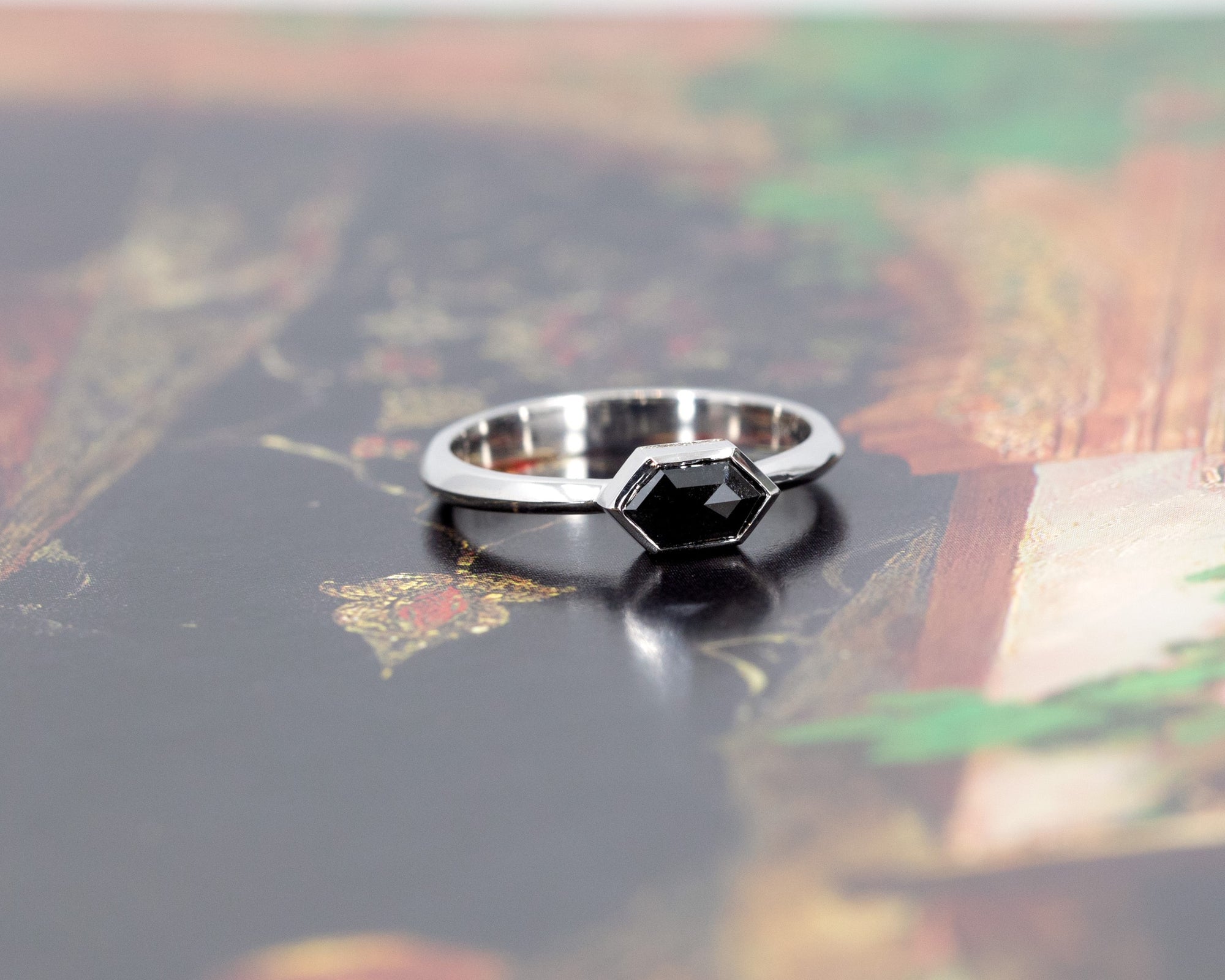 Modern black diamond ring in white gold, displayed on a vibrant colored background, crafted with precision and creativity by Bena Jewelry, a designer jeweler based in Montreal.