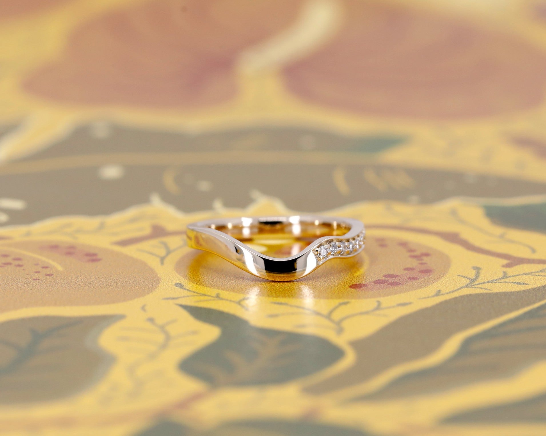 Sculptural yellow gold wedding band with diamonds shown against a deep brown backdrop. Refined, asymmetric design by Bena Jewelry, Canadian fine jewelry label.