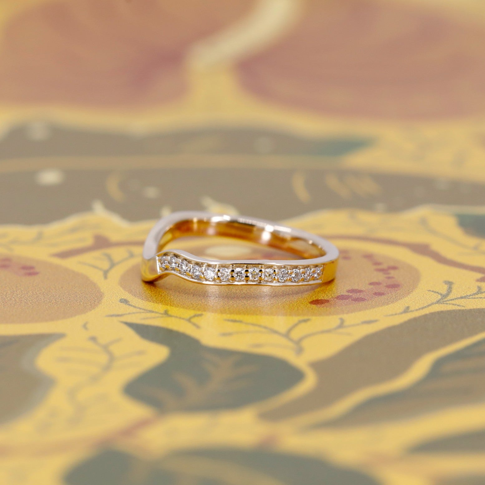 Curved yellow gold diamond ring styled on a warm brown background. The elegant pavé diamonds follow the wave silhouette. Fine contemporary jewelry by Bena Jewelry, Montreal.