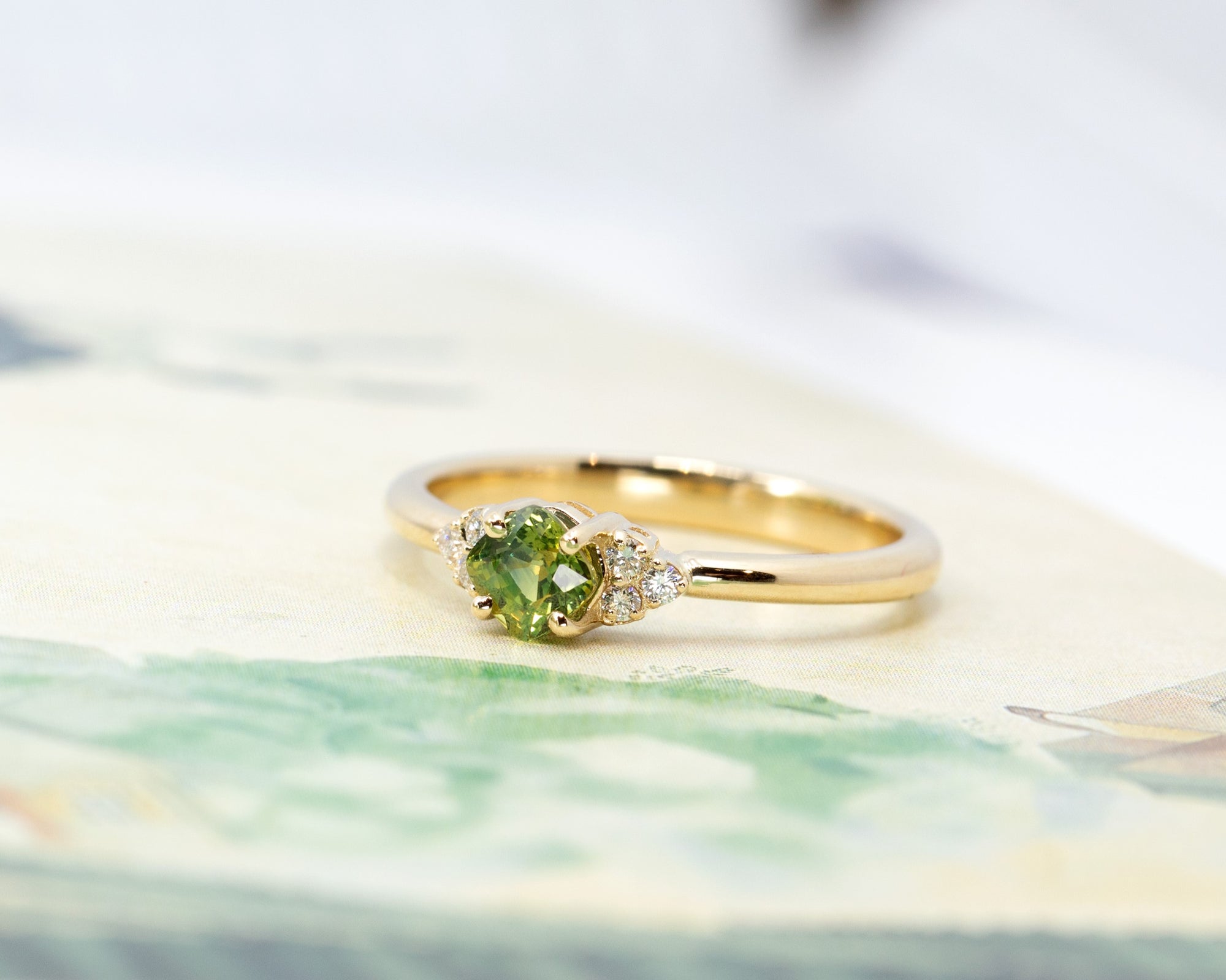 Elegant green sapphire ring with a cushion-cut gemstone and sparkling side diamonds. A modern and refined engagement ring by Bena Jewelry, crafted in Montreal.