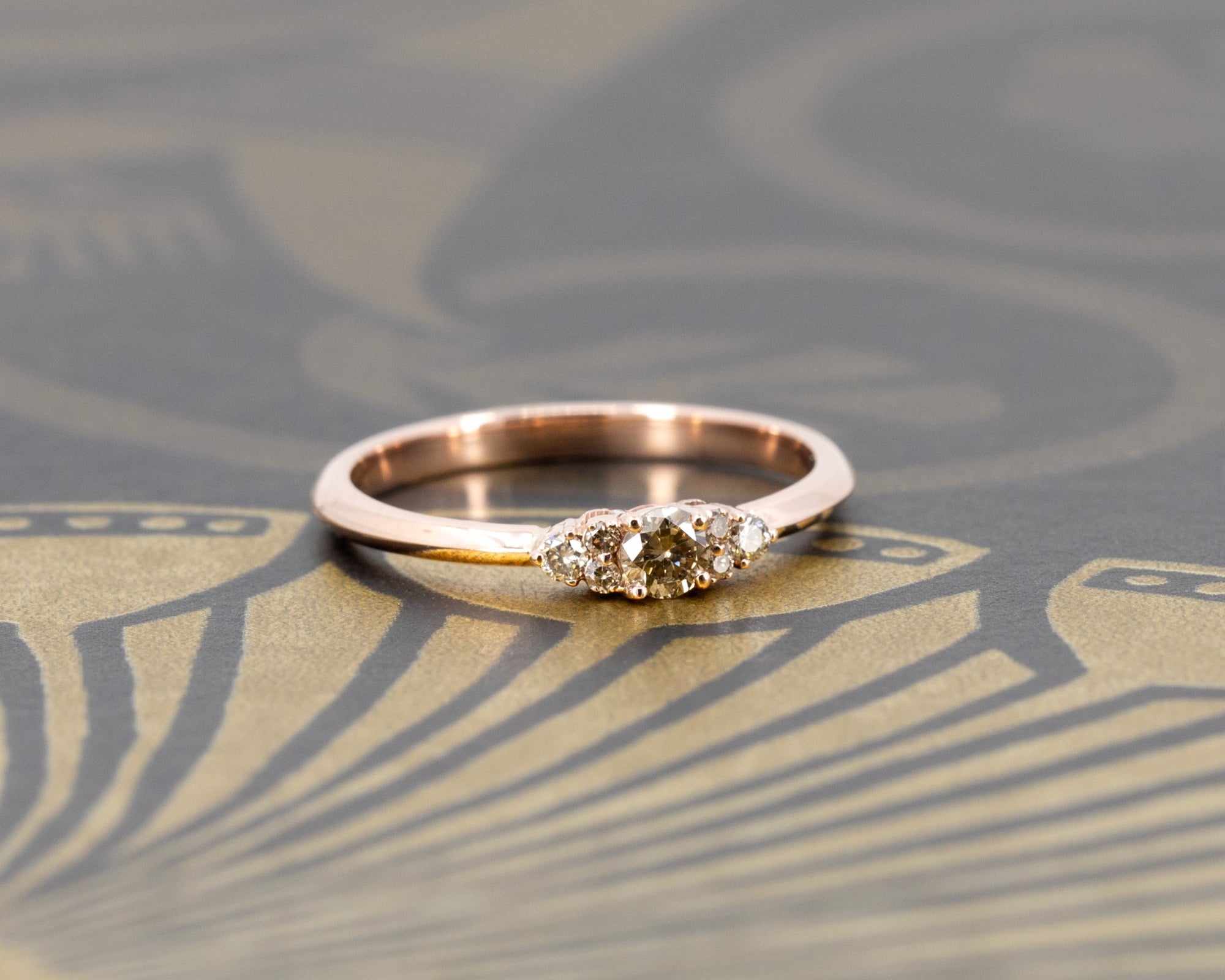 Elegant engagement ring by Bena Jewelry, featuring a champagne diamond and side stones, set in rose gold. Highlighted against a deep dark background, showcasing its brilliance and sophistication. Handmade in Montreal.
