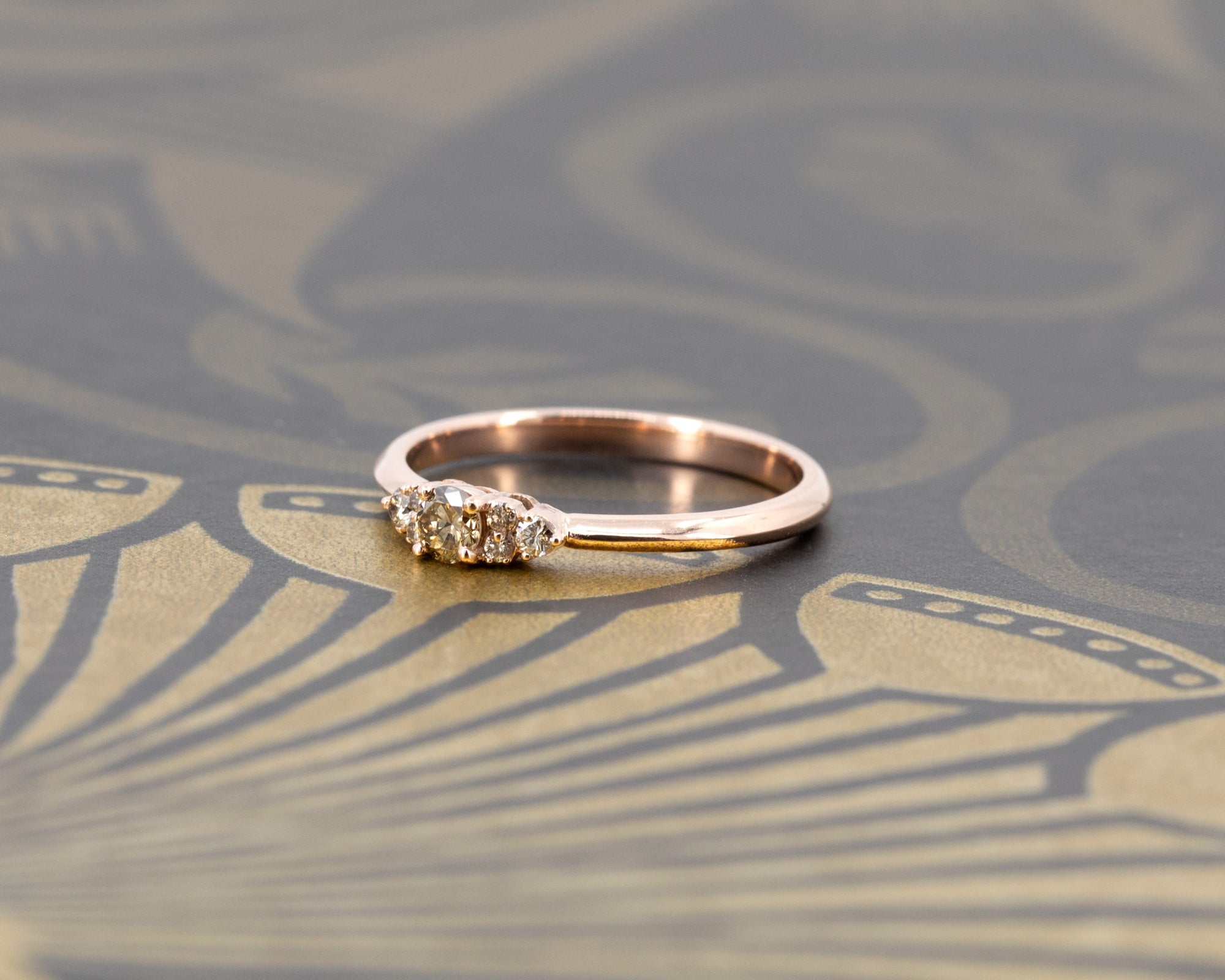 Bena Jewelry’s custom rose gold engagement ring with a golden champagne diamond and sparkling side stones. Photographed on a dark matte surface for a bold and luxurious look. Designed and crafted in Montreal.