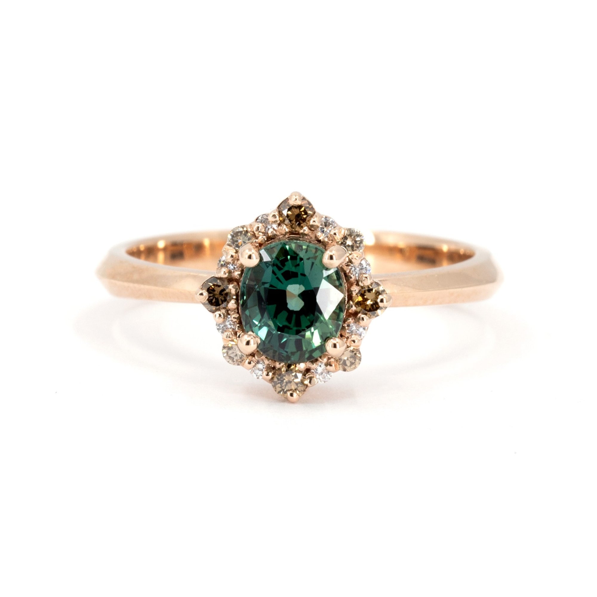 Close-up of a rose gold ring featuring an oval teal sapphire with a halo of brown and white diamonds, designed by Bena Jewelry in Montreal.