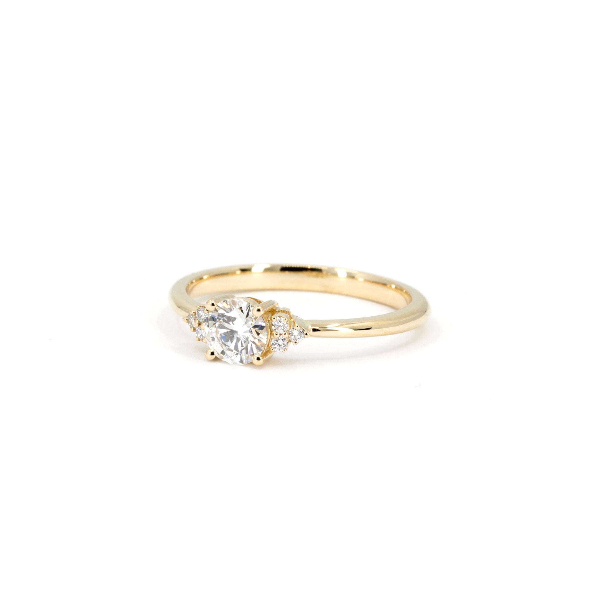 Classic yellow gold engagement ring with a central round diamond and sparkling side stones by Bena Jewelry displayed on a white background bridal jewelry made in Canada