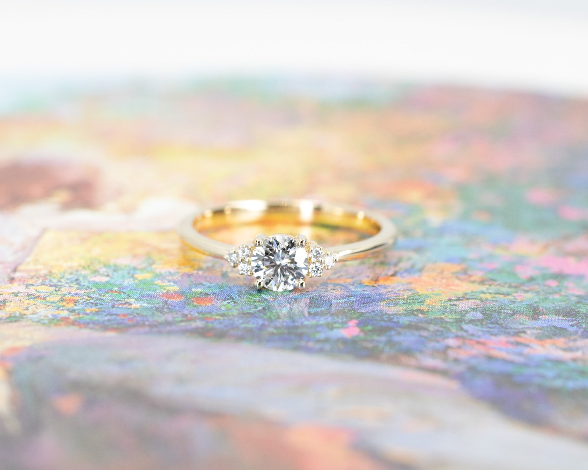 Yellow gold Round Diamond Desir Ring with a round-cut diamond and side stones by Bena Jewelry displayed on a soft pastel background custom bridal ring Montreal