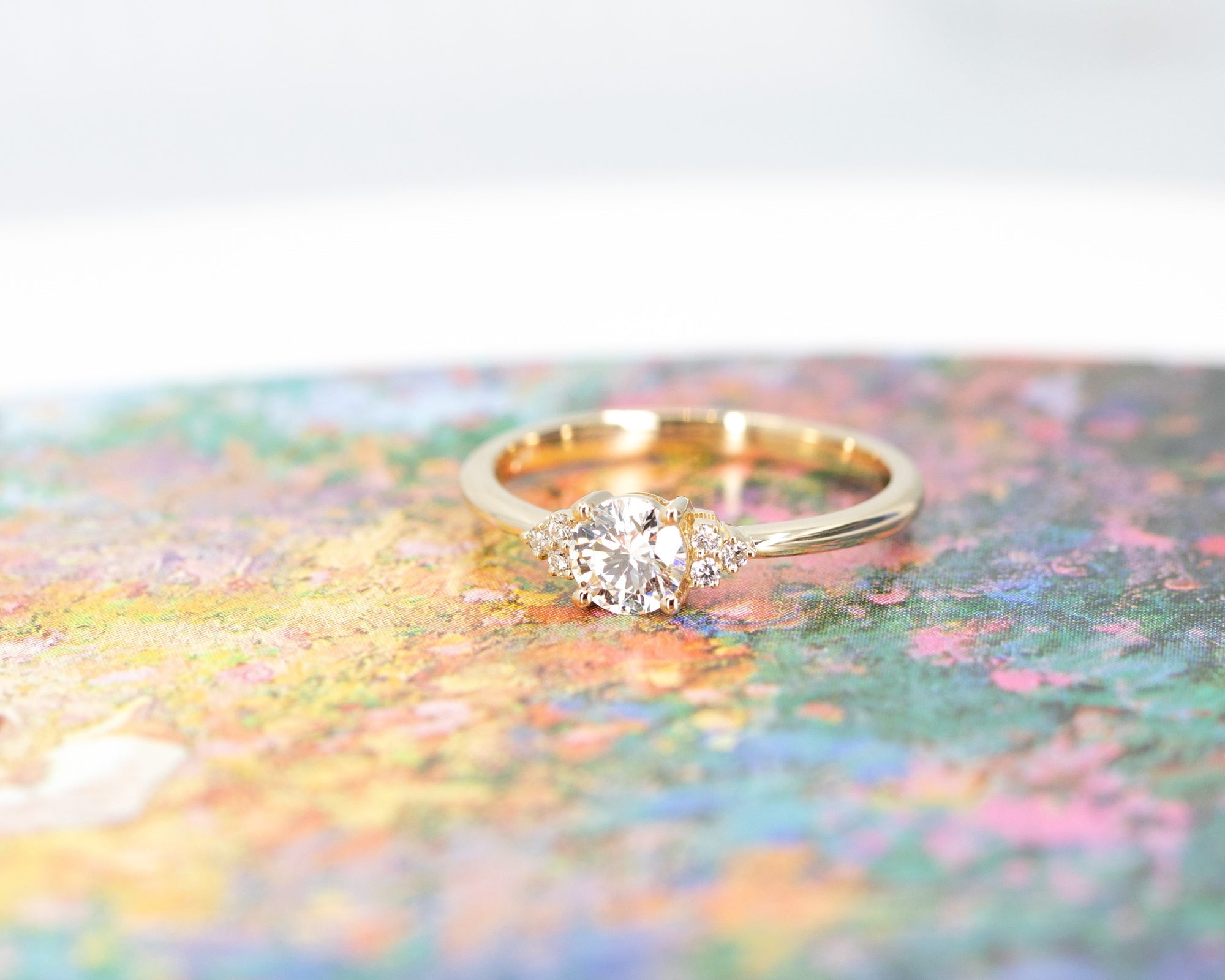 Elegant yellow gold engagement ring featuring a round diamond and side accents Round Diamond Desir Ring by Bena Jewelry photographed on a vibrant colored backdrop