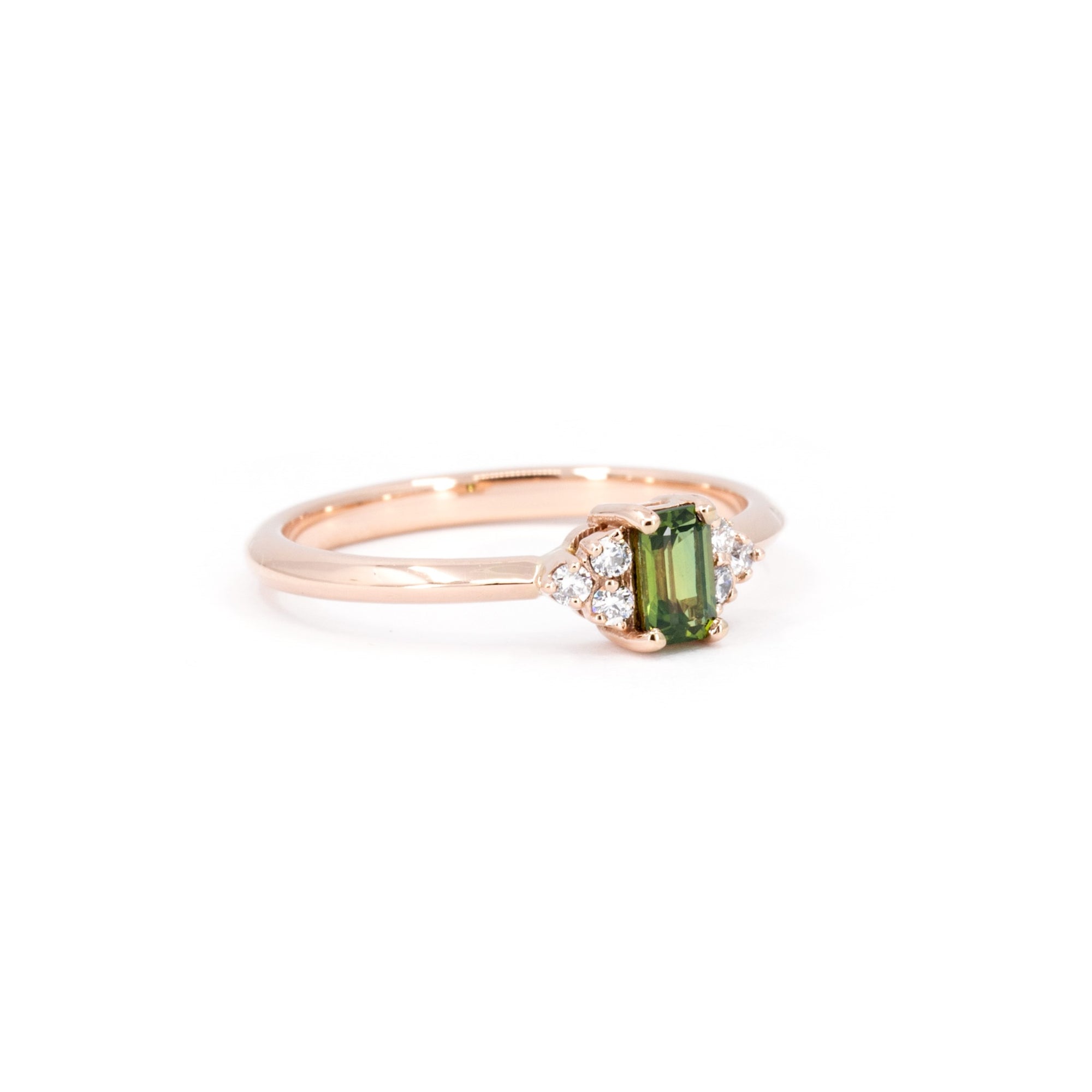 Rose gold engagement ring with a baguette-cut green sapphire and round diamonds Désir Ring by Bena Jewelry displayed on a white background fine bridal jewelry in Canada