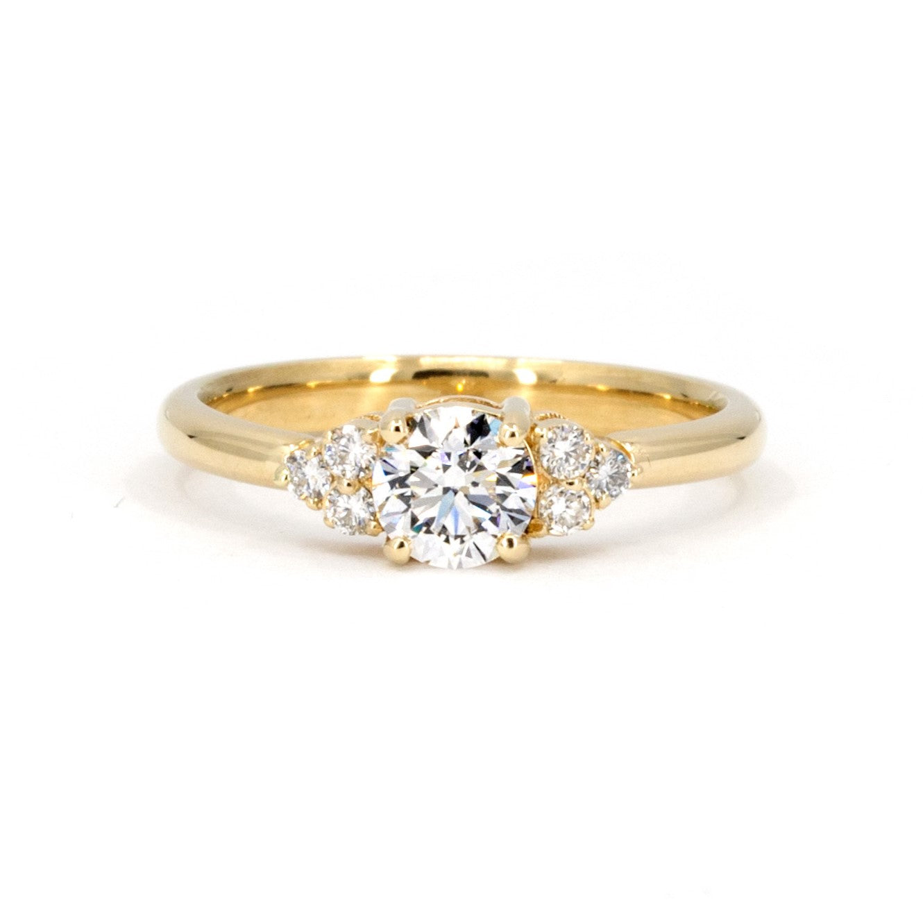 Yellow gold engagement ring featuring a central round diamond and side stones, custom-made by Bena Jewelry in Montreal, Canada. Timeless fine jewelry.