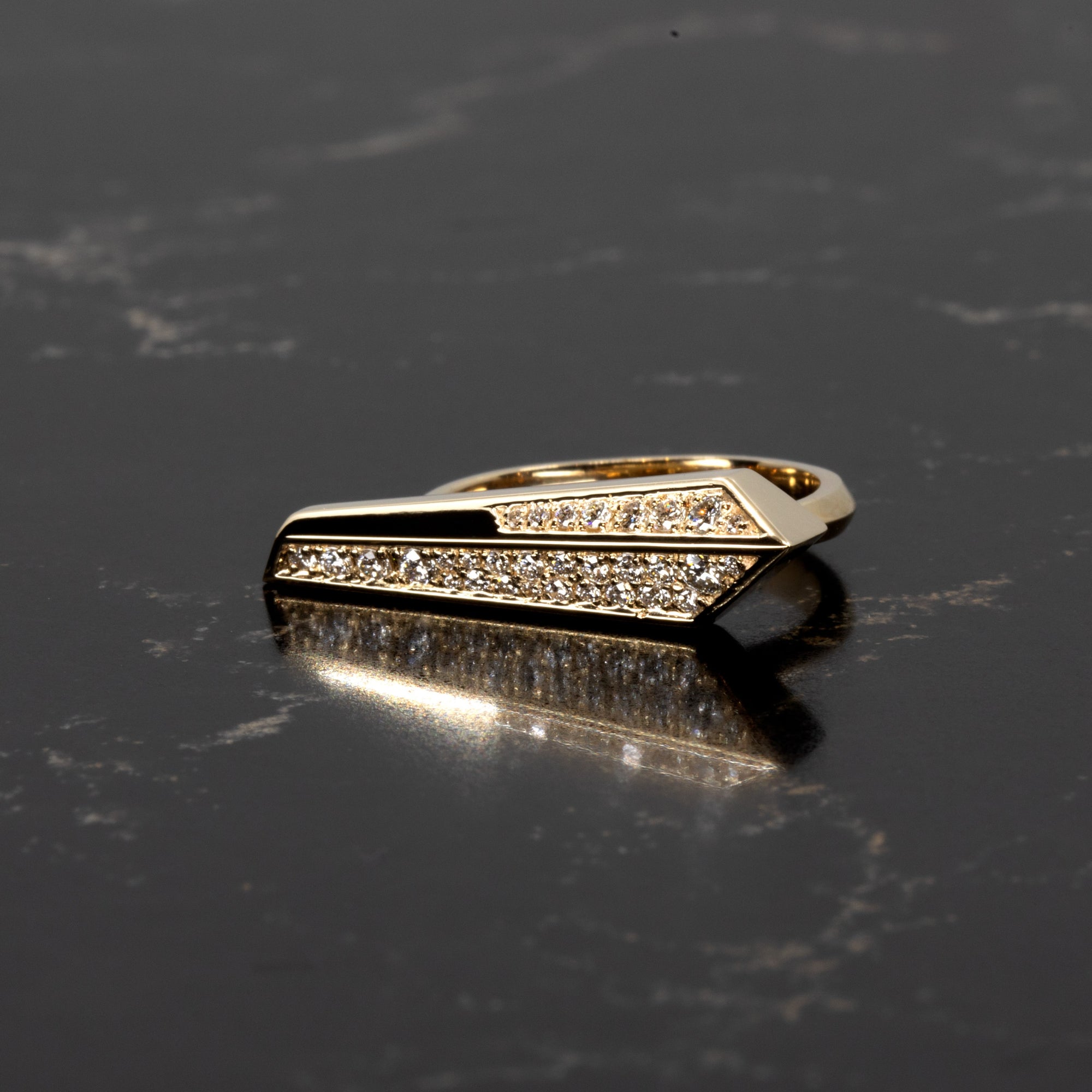 Moody lighting on a geometric diamond ring by Bena Jewelry, crafted in Montreal in 14k yellow gold with pavé diamonds, shown on black backdrop.