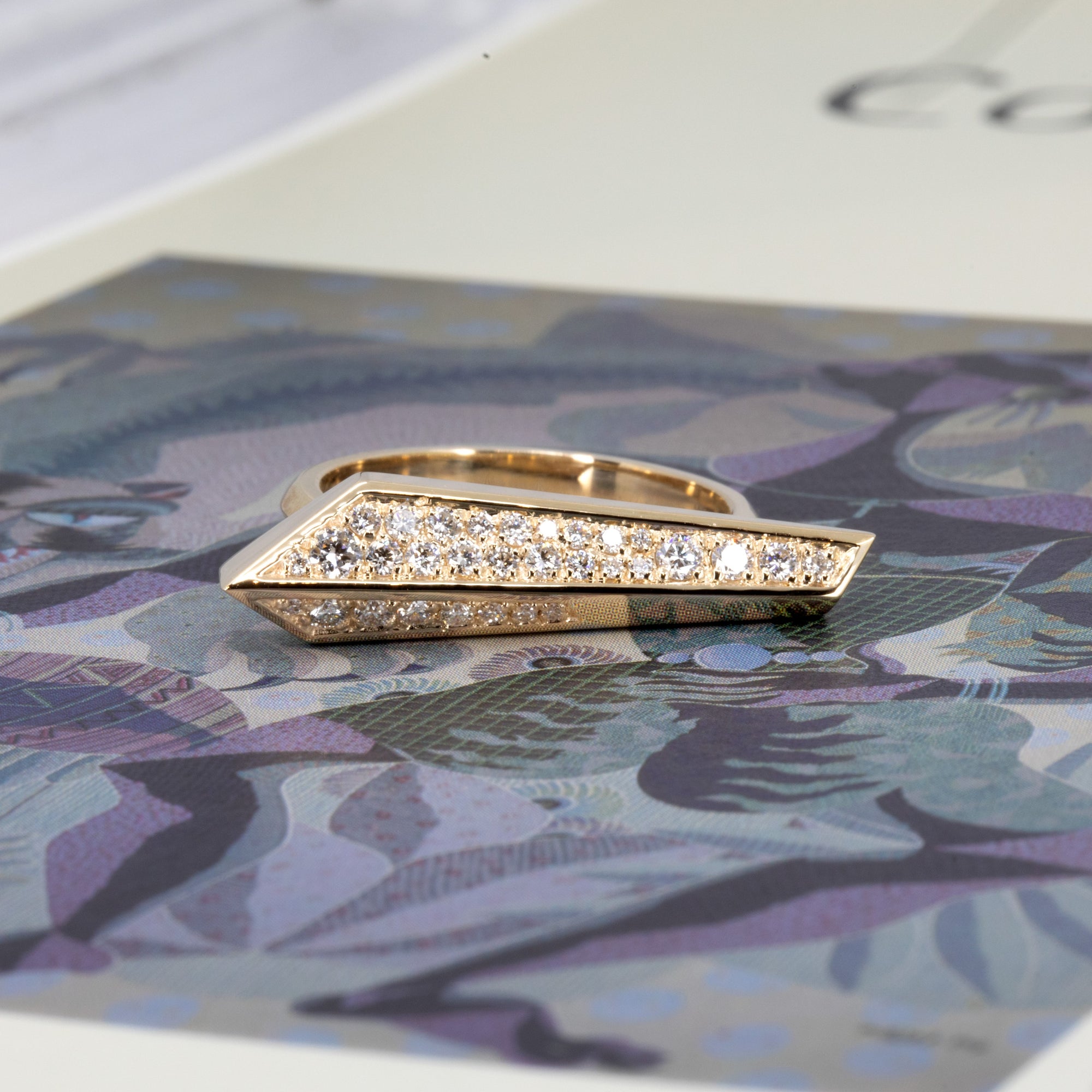 Gold and diamond ring with graphic lines by Bena Jewelry, Montreal-based designer, shown on a bold color backdrop for a contemporary look.