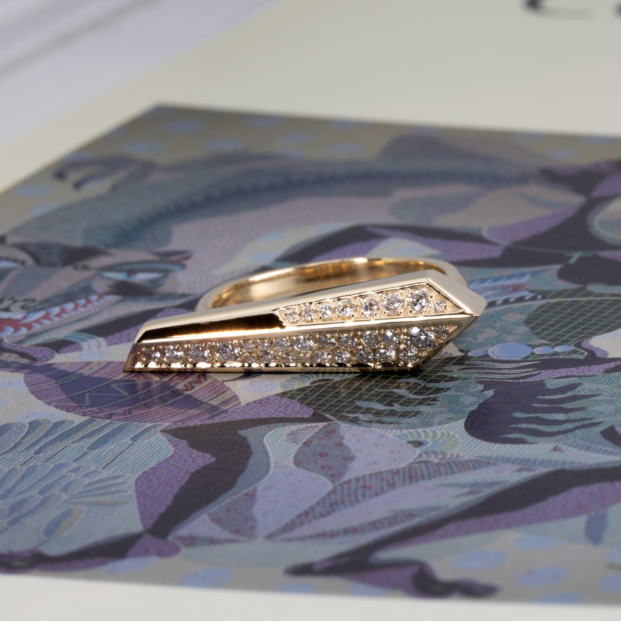 Edgy Bena Jewelry ring with pavé-set diamonds photographed on a vibrant colored background, emphasizing the contrast and sharp form of the gold design.