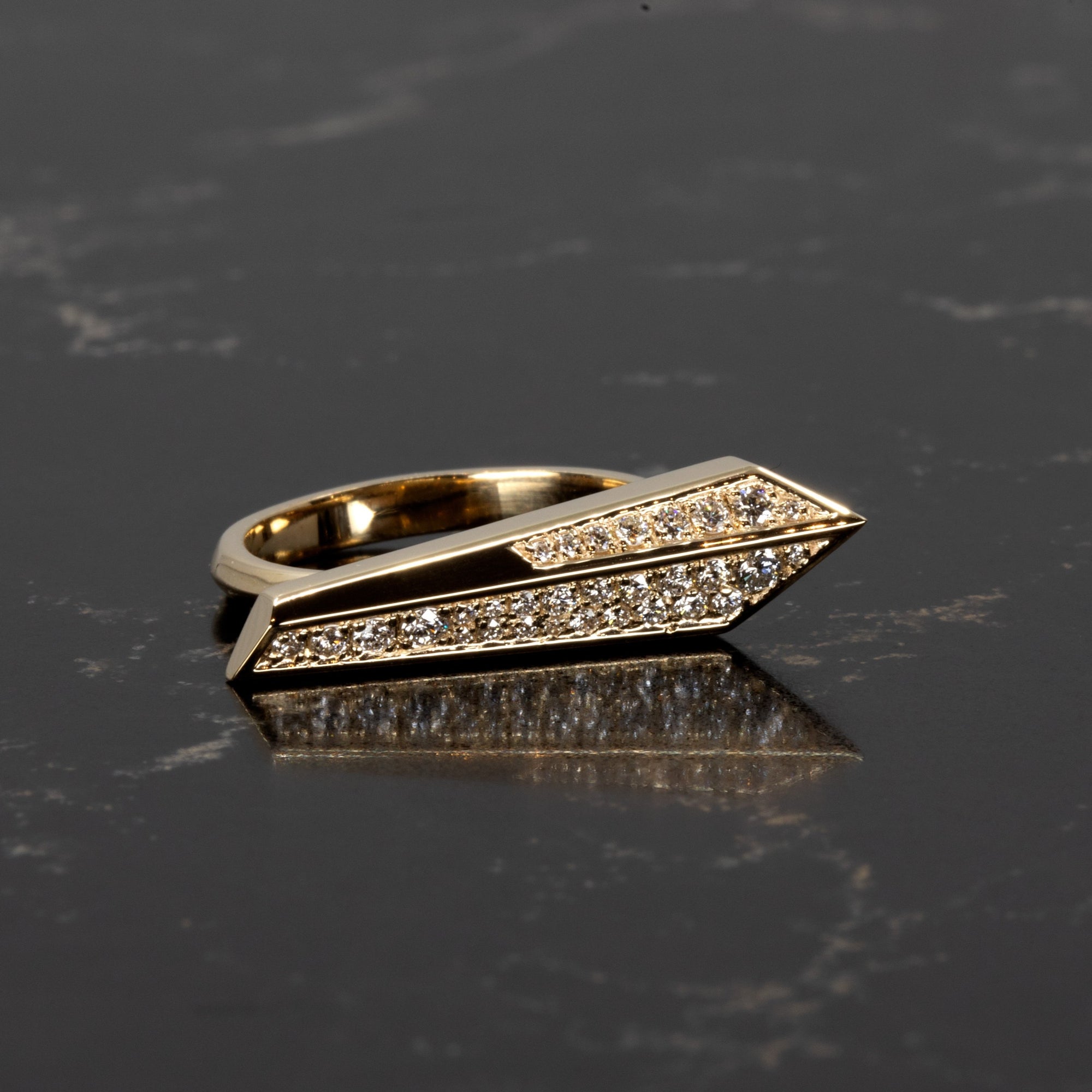 Contemporary gold ring with sharp silhouette and pavé diamonds, handmade by Bena Jewelry in Montreal, photographed against a deep-toned surface.