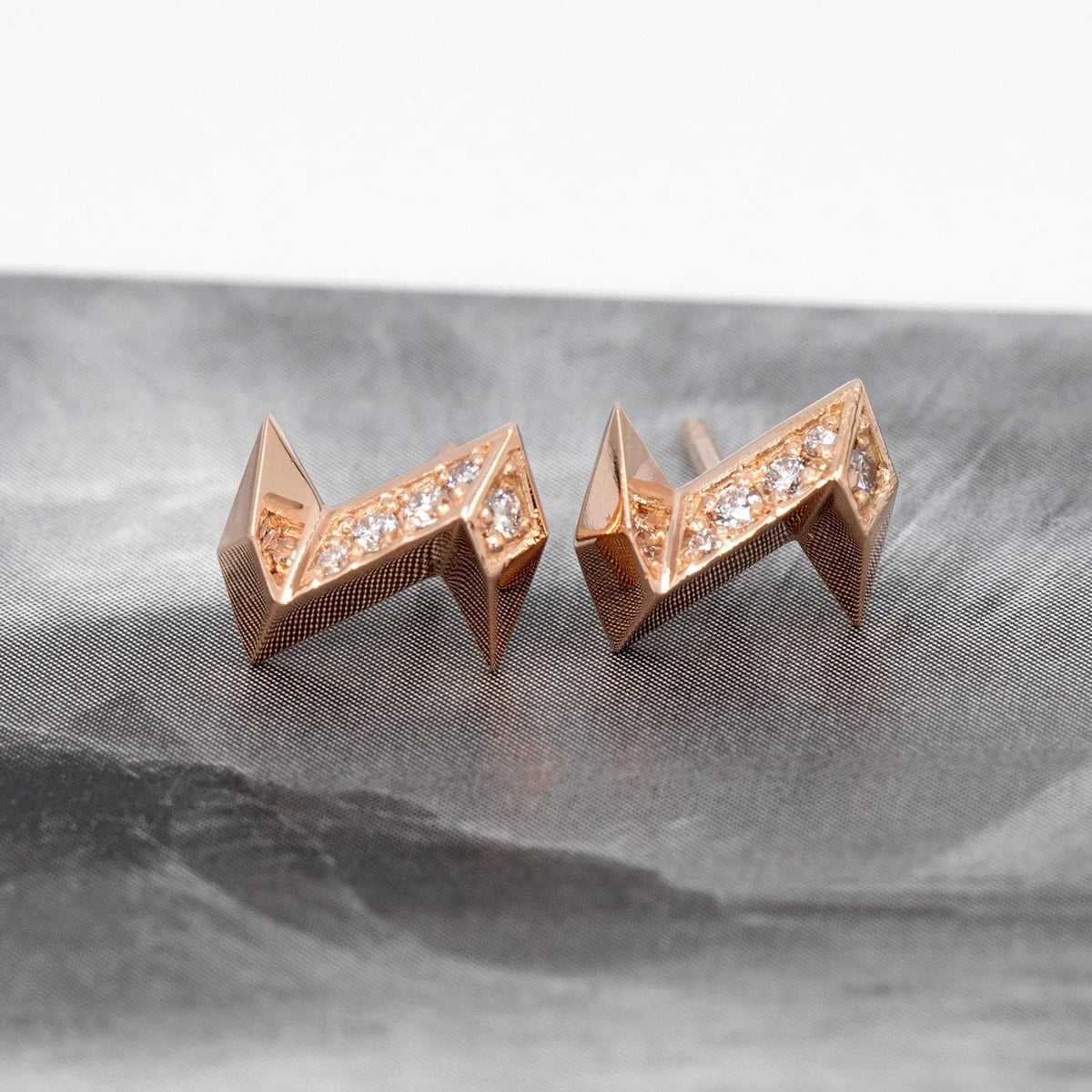 Earrings in 14-carat rose gold with lab-grown diamonds. The pair of lightning bolt earrings is photographed in an abstract black and white image. The detail of the print is reflected on the polished surface of the gold earrings. This slightly punk and offbeat piece of jewelry can be both very chic and just as appropriate for casual wear. 