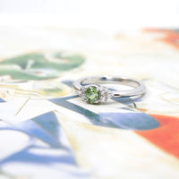 side view of bena jewelry colored gemstone engagement ring with demantoid green garnet and natural diamond white gold ring made in montreal by bena jewelry available at ruby mardi on mulit color background