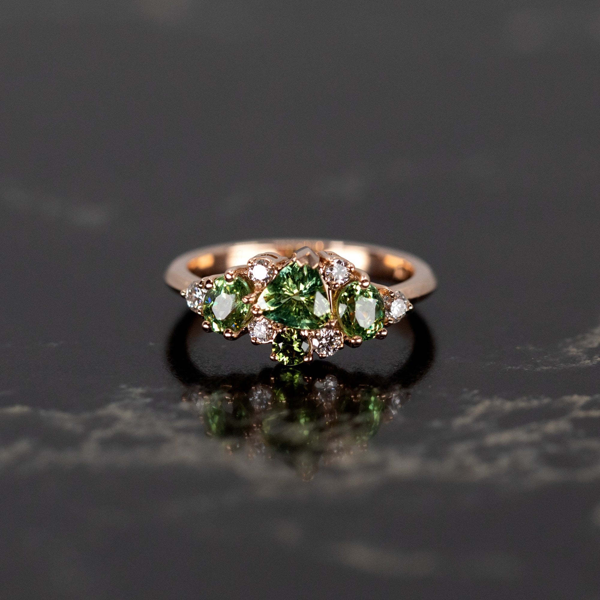 Designer ring with green sapphire and demantoid garnets, set in rose gold, photographed on a bold dark background. Crafted by Bena Jewelry in Montreal.