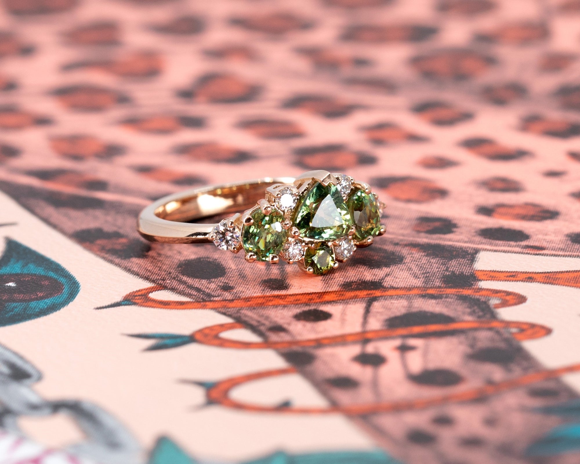 Green sapphire and demantoid garnet ring in rose gold, displayed on a vibrant colored background. Made by Bena Jewelry in Montreal.