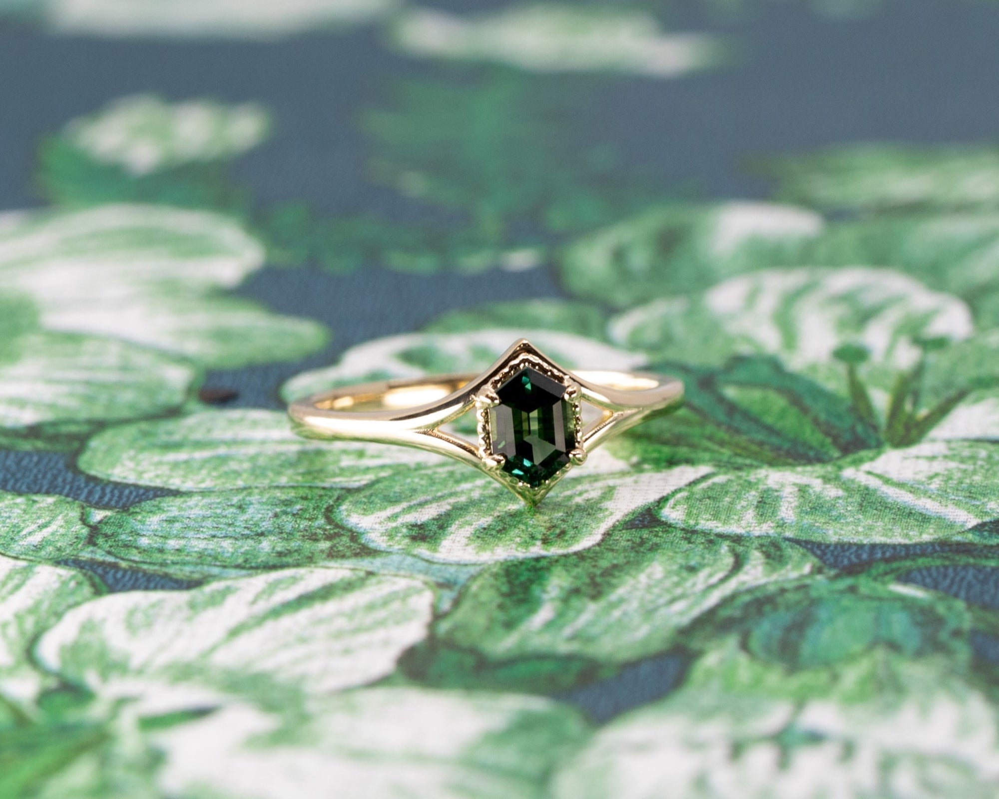 Close-up of the Adorn Hexagonal Green Sapphire Ring’s hexagonal sapphire, with intricate detailing on the yellow gold band. Made by Bena Jewelry, a bespoke creation from Montreal, Canada.