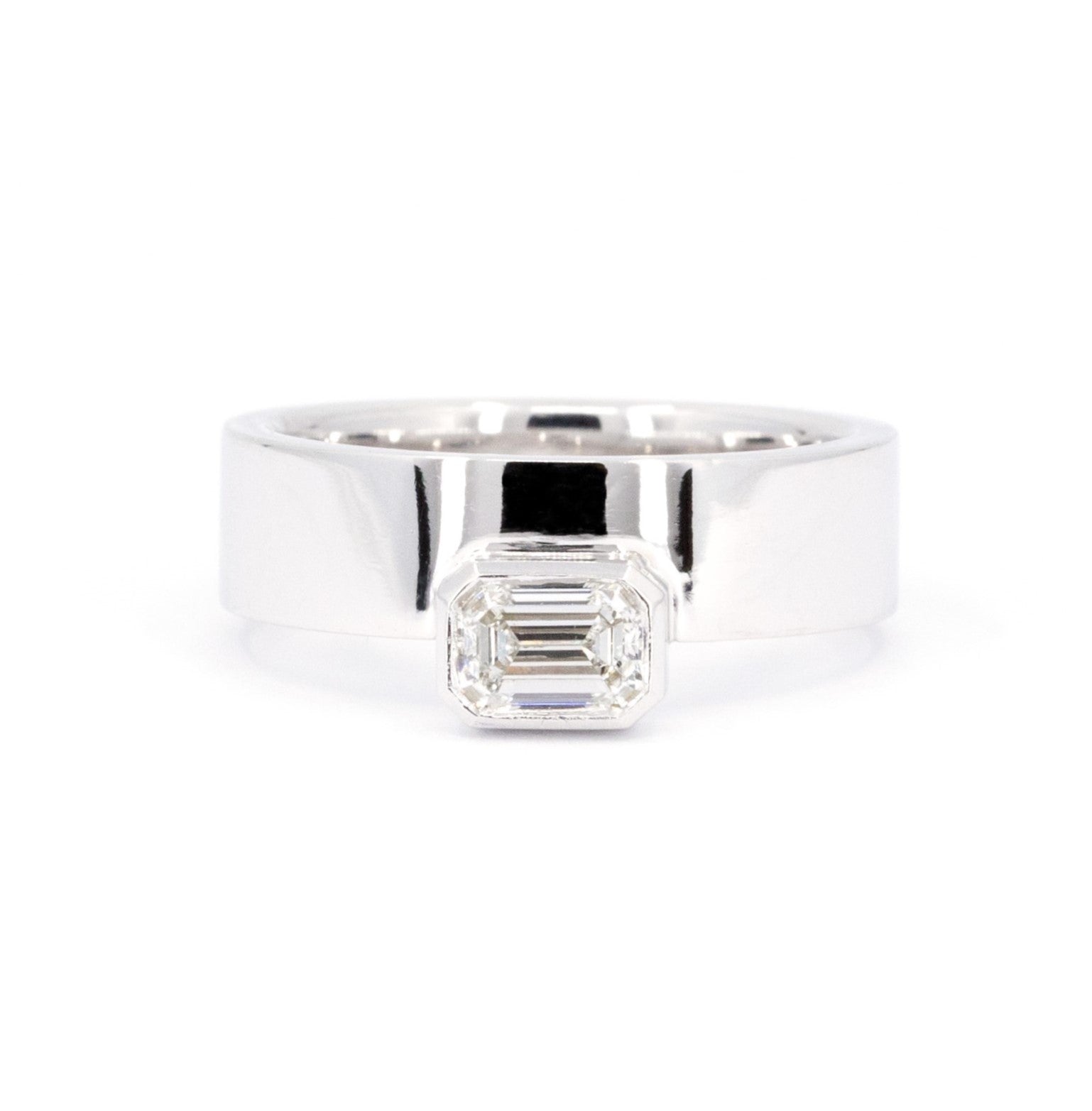 Wide and bold unisex white gold band featuring a bezel-set emerald-cut diamond. Designed by Bena Jewelry, this statement piece offers a boxy, modern style with a sleek and stylish look. Photographed on a white background.