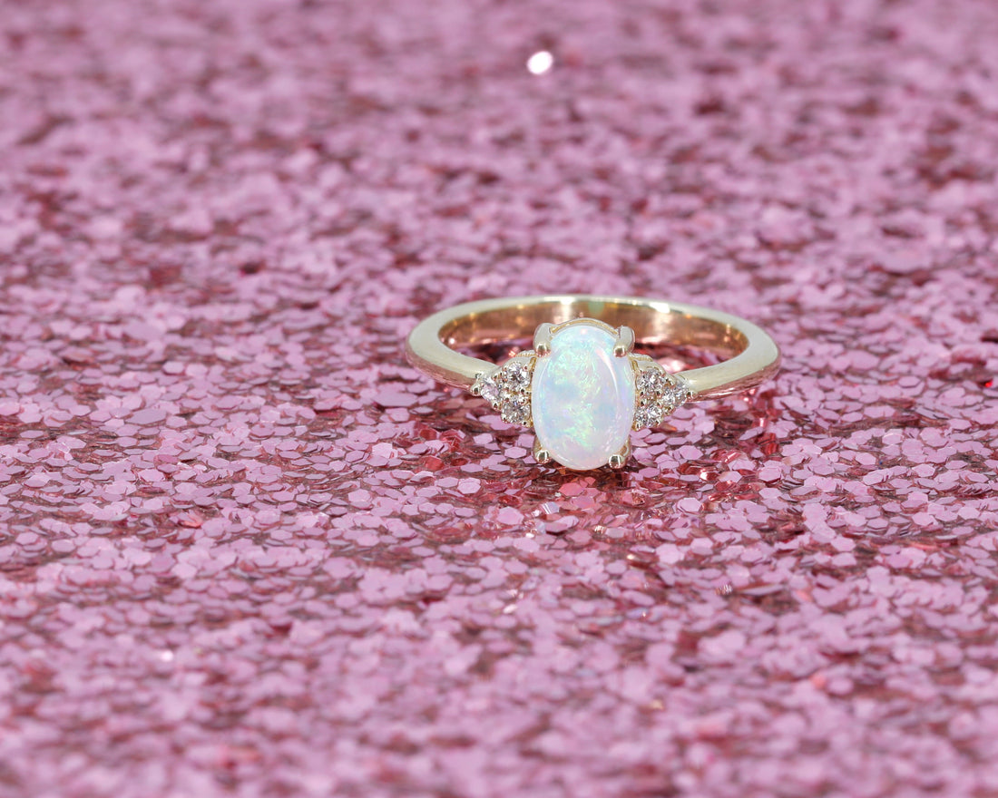 oval shape opal germstone and diamond dainty engagement ring custom made in motnreal by bena jewelry designer on pink glitter background