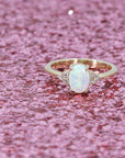 oval shape opal germstone and diamond dainty engagement ring custom made in motnreal by bena jewelry designer on pink glitter background