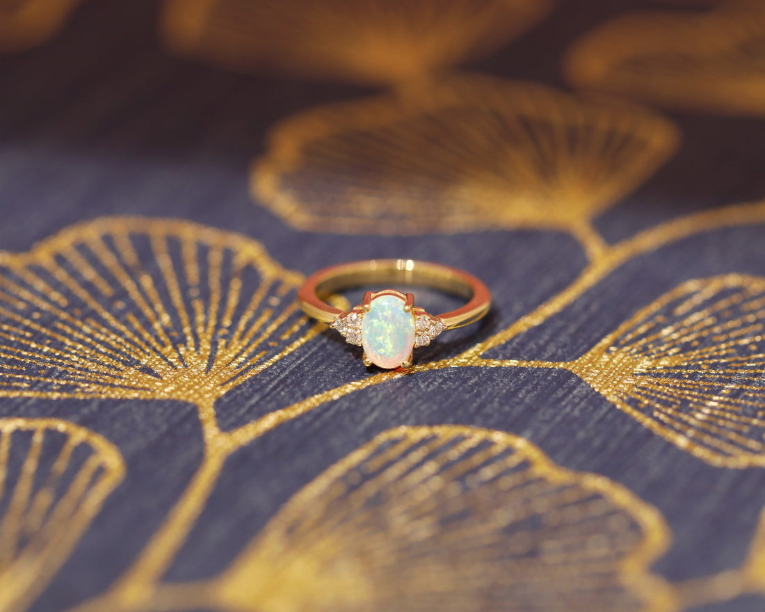 front view of oval shape opal gemstone and diamond on yellow gold engagement ring by bena jewelry on multi color background