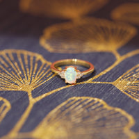 front view of oval shape opal gemstone and diamond on yellow gold engagement ring by bena jewelry on multi color background