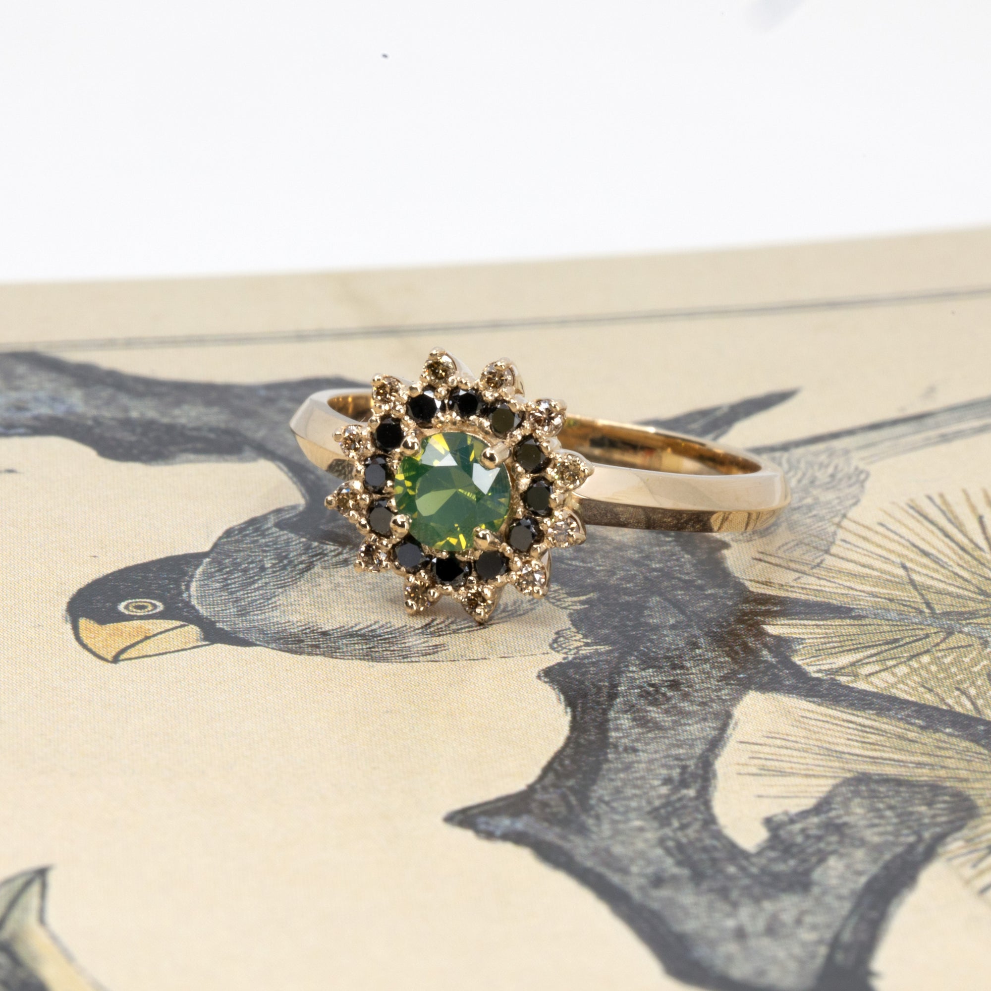 Artistic shot of a Bena Jewelry green sapphire and diamond ring on a colorful backdrop, showcasing the contrast of black and brown diamonds against 14k gold, made in Montreal.