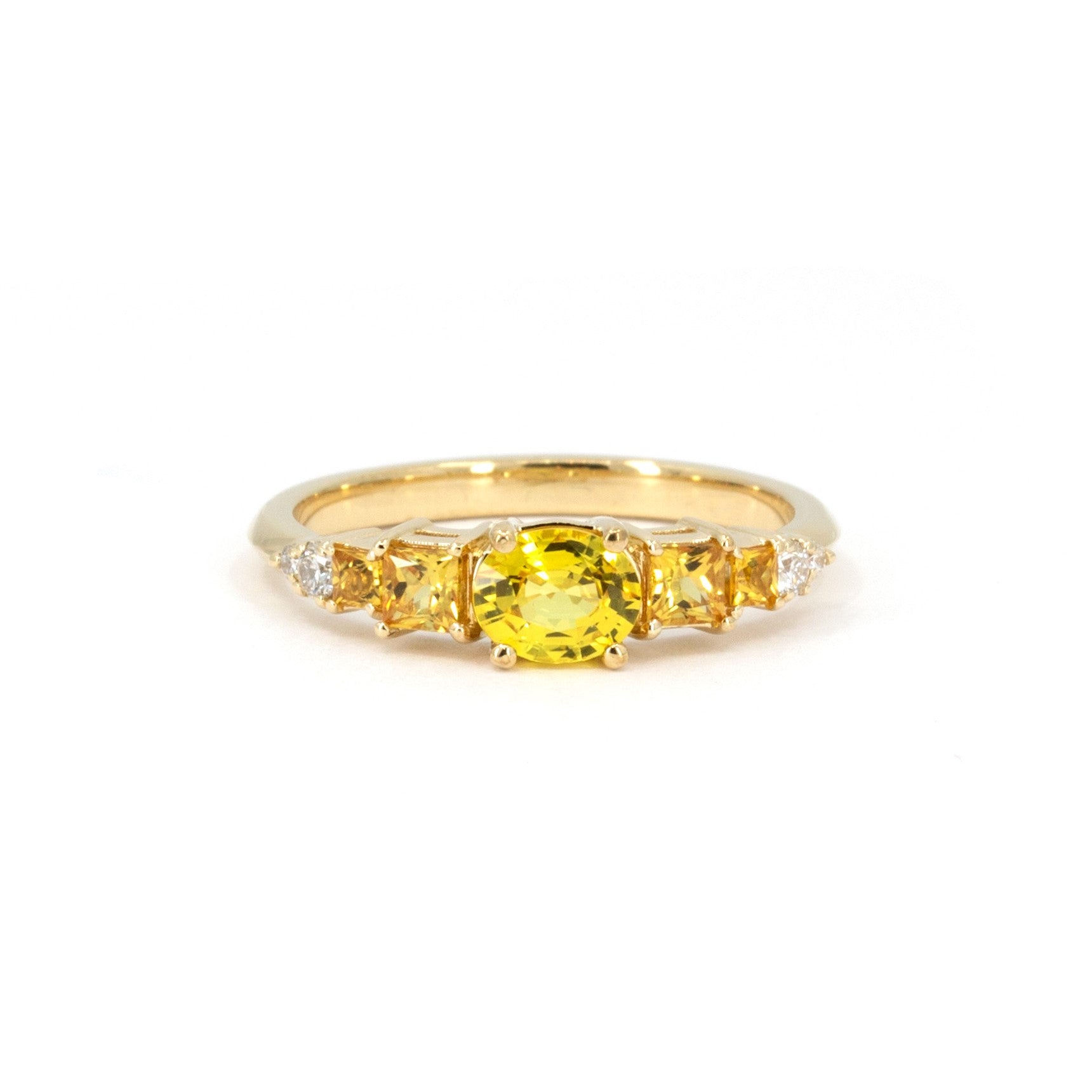 Yellow gold engagement ring by Bena Jewelry, featuring a vivid yellow oval sapphire center stone, flanked by orange princess cut sapphires and diamonds, displayed on a white background.