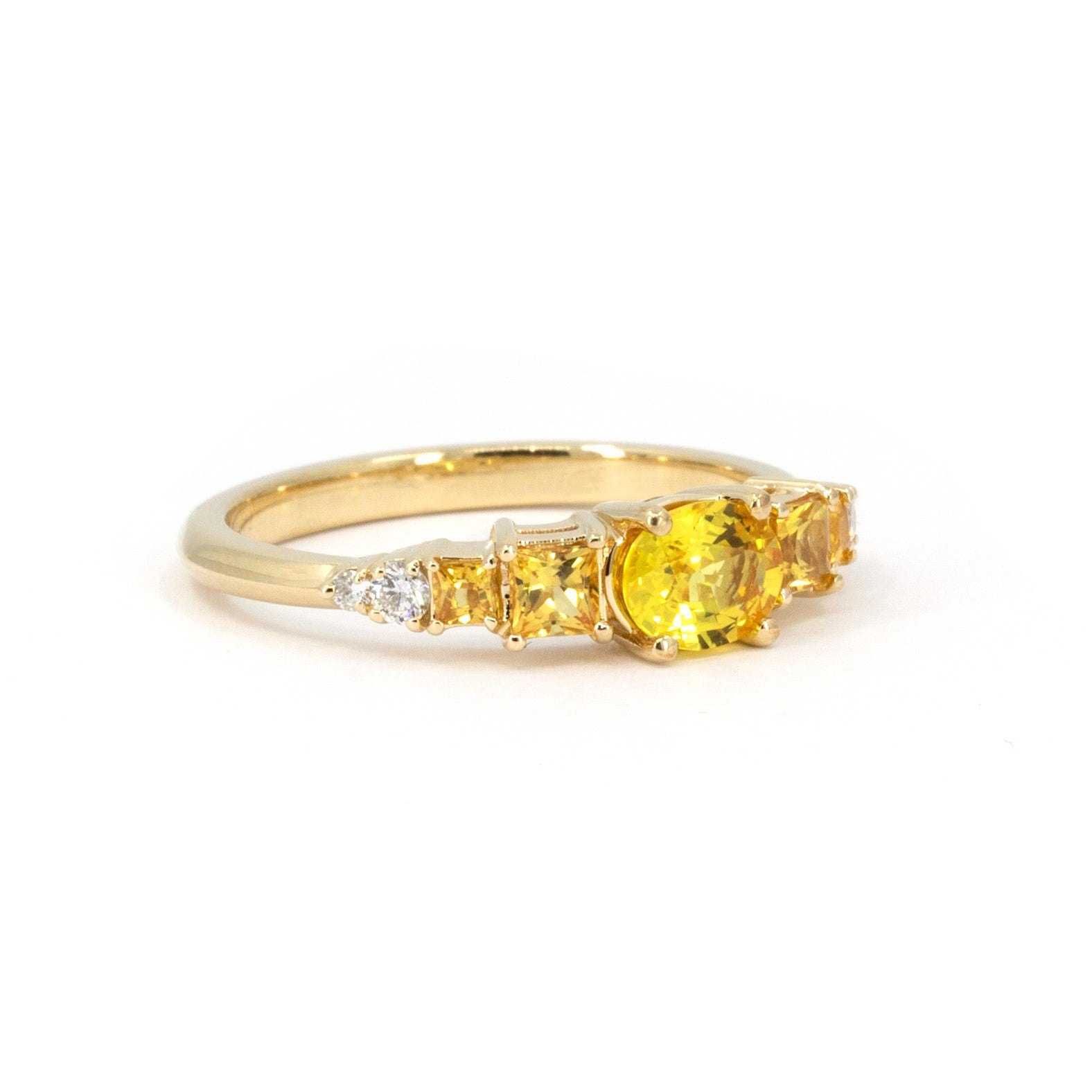 Close-up of Bena Jewelry&#39;s yellow gold engagement ring, highlighting the vivid yellow oval sapphire center stone, orange princess cut sapphires, and diamond accents, set against a white background.