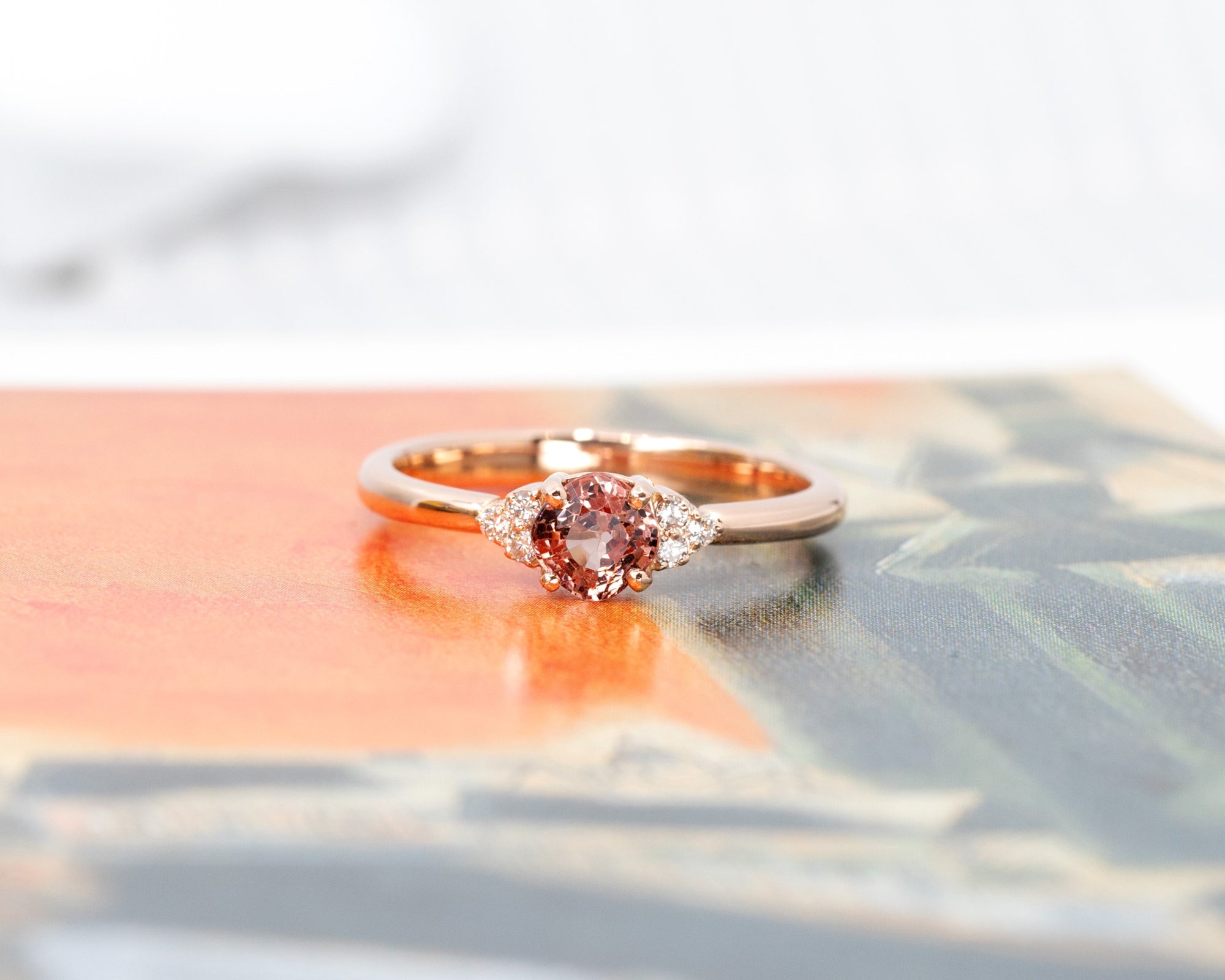 Elegant engagement ring with a peach spinel and diamond accents, displayed on a soft-hued background to enhance its warmth and brilliance. Handmade in Montreal.