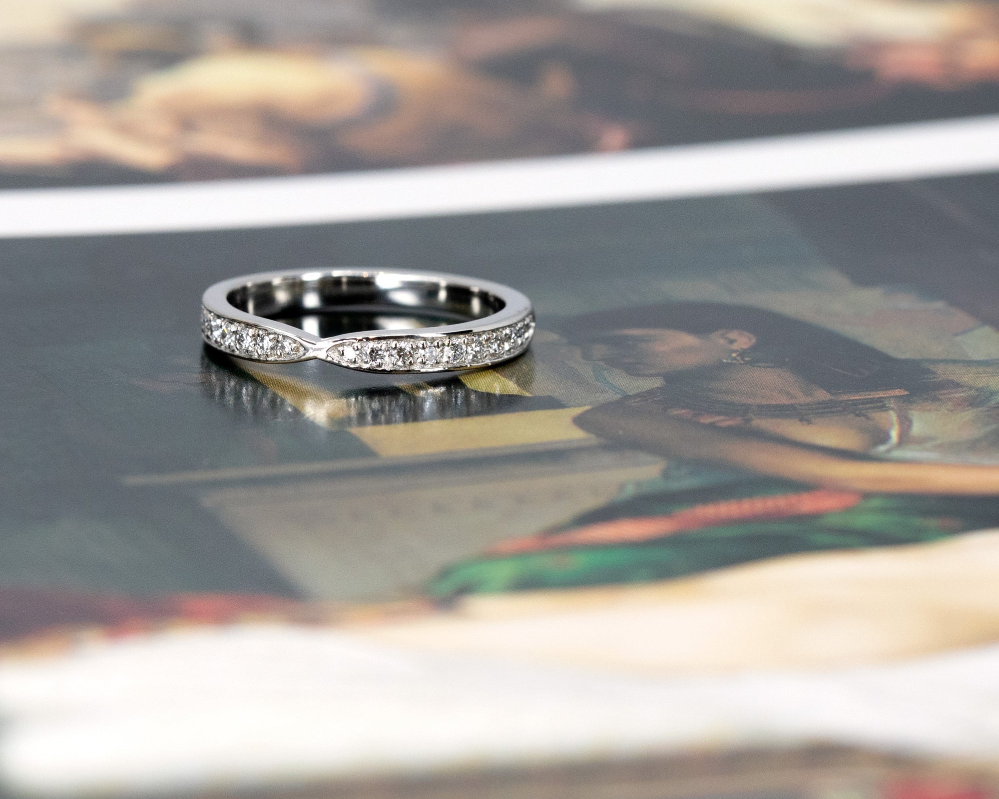 Elegant pinch-designed platinum wedding ring with sparkling diamonds, set against a bold colored backdrop. Crafted by Bena Jewelry, Montreal, Canada.