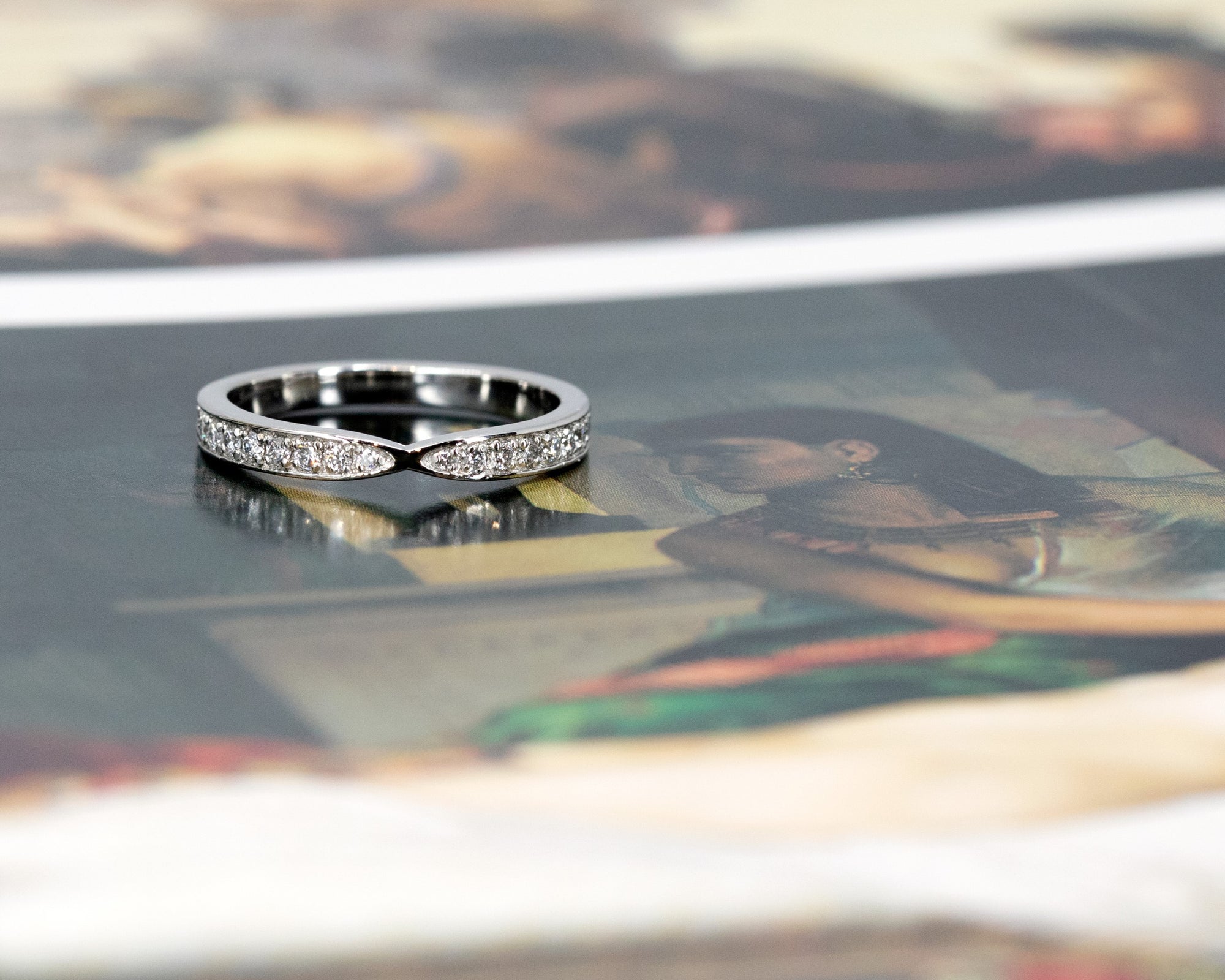 Front view of a designer bridal platinum band with a pinch detail and diamonds, displayed on a vibrant background. Custom-made by Bena Jewelry in Montreal.