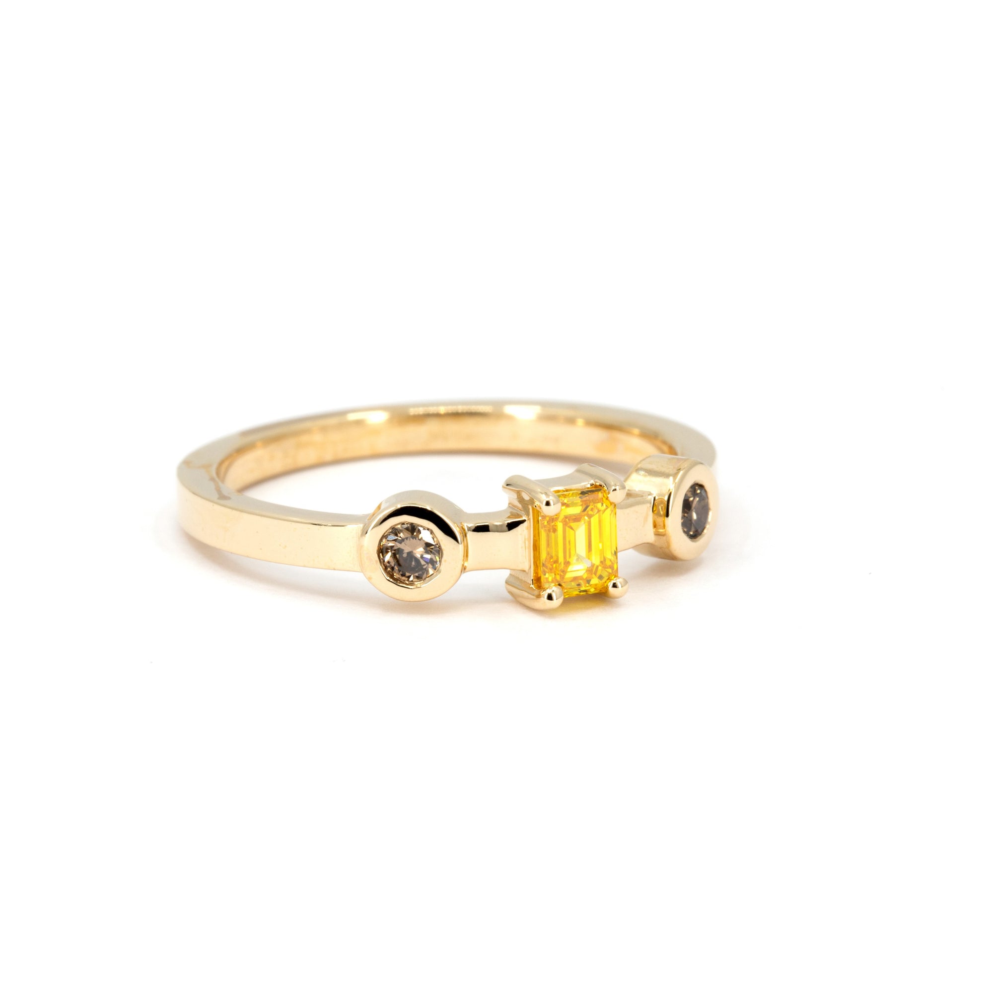 Front-facing image of a contemporary yellow gold ring with a vibrant yellow emerald-cut diamond and two brown accent diamonds, captured on a white backdrop.
