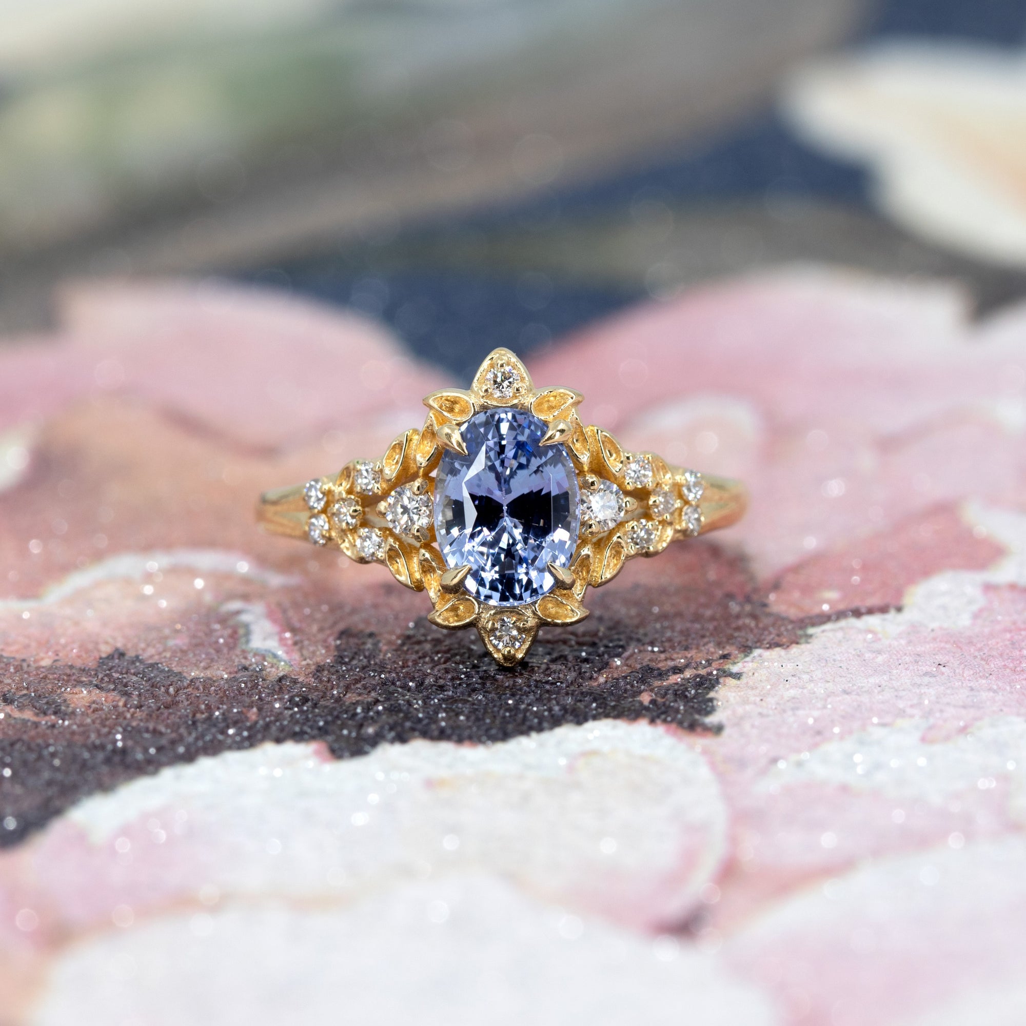 Sky Bloom Sapphire Ring on soft-toned background – The luminous blue sapphire and floral gold details contrast beautifully with the subtle backdrop.