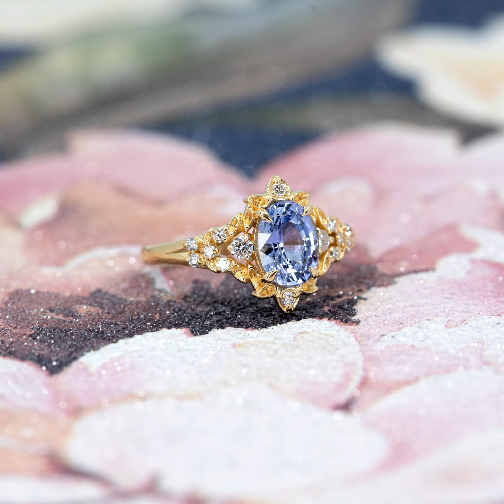 Close-up of engagement ring on dark background – The intricate floral gold setting highlights the brilliance of the sapphire in a dramatic way.