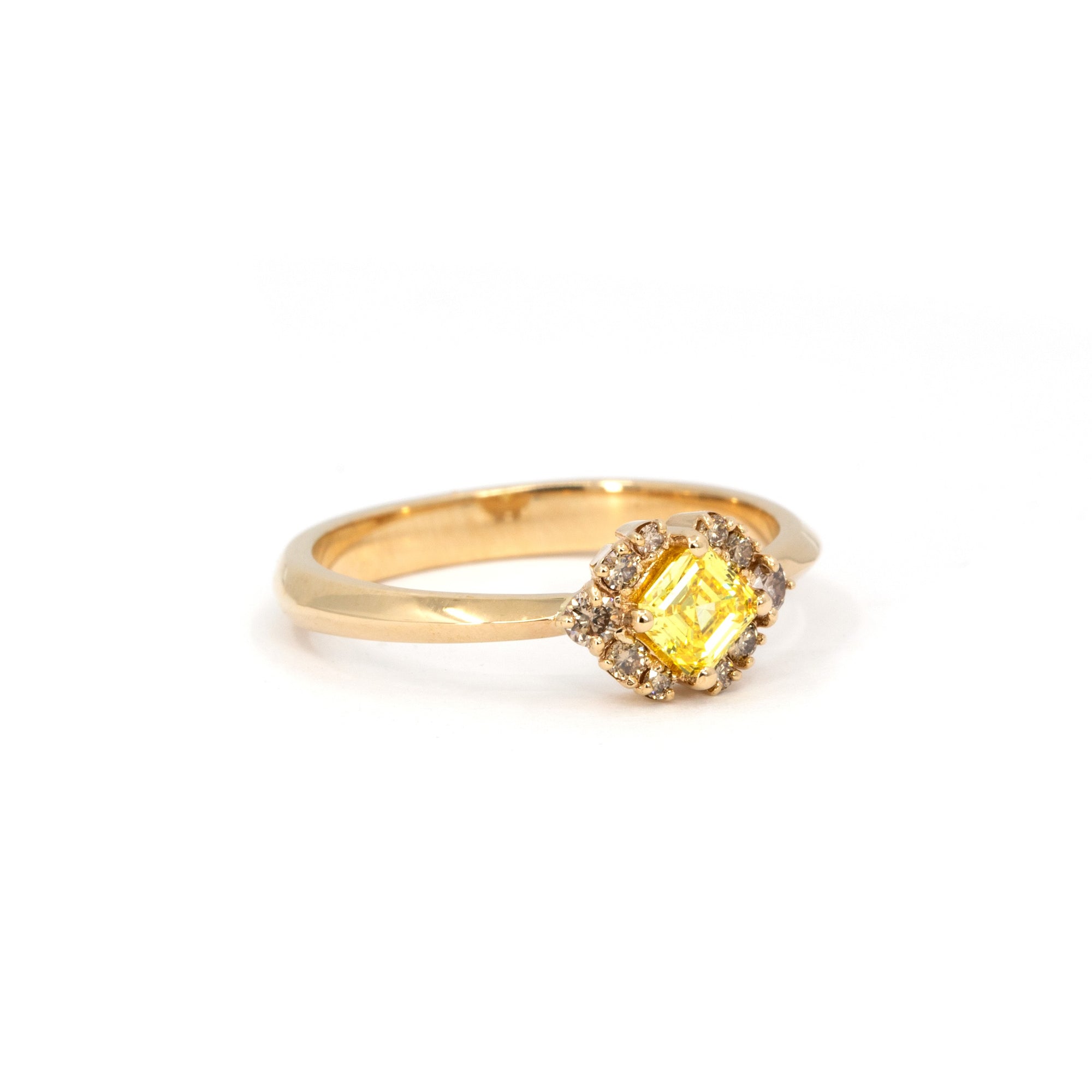 Minimalist product shot of a yellow Asscher diamond ring surrounded by brown diamonds, made by Bena Jewelry in Montreal, shown on a neutral white backdrop.