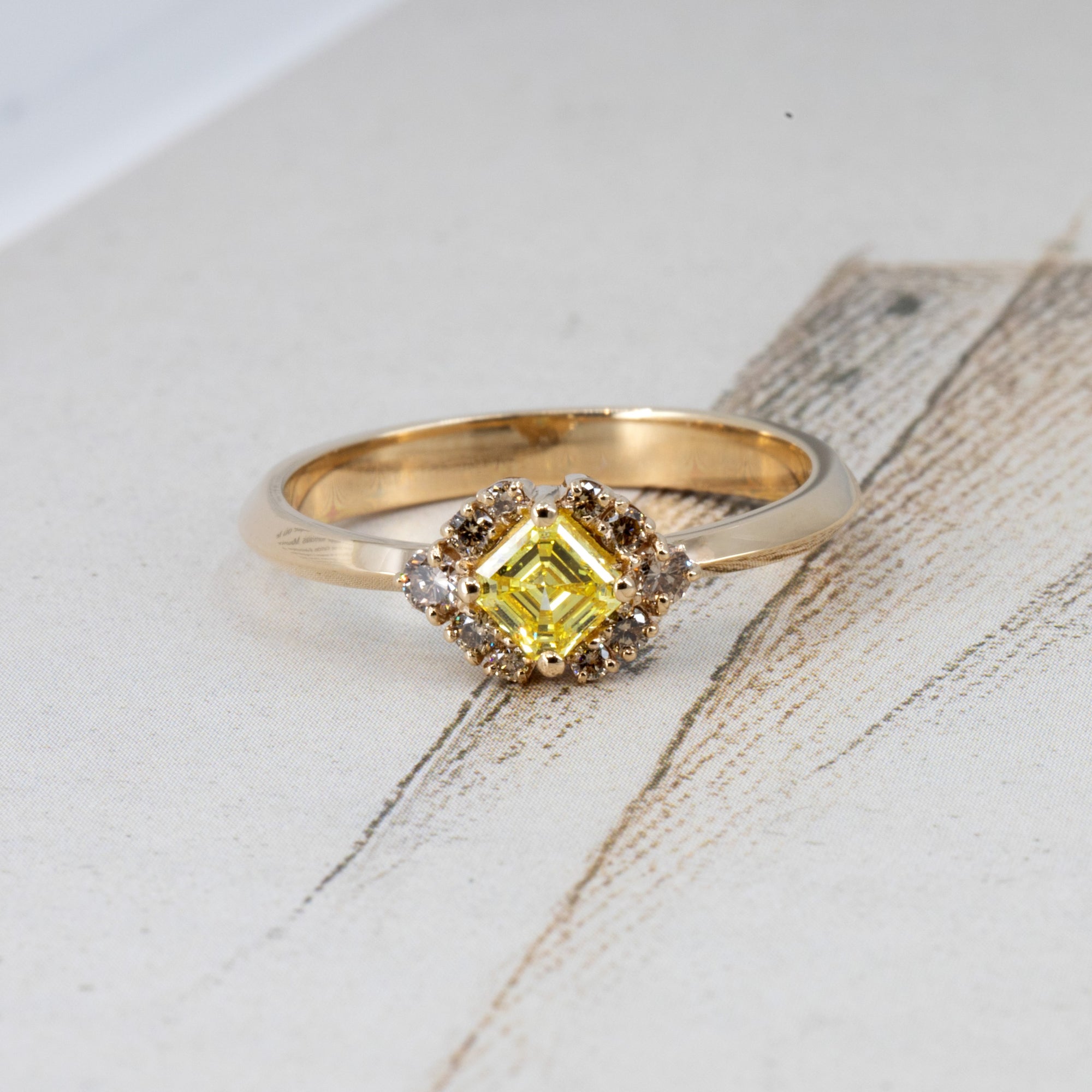 Creative flatlay of a contemporary Bena Jewelry ring with a yellow Asscher diamond and brown halo, made in Montreal, displayed on a colorful background for visual impact.