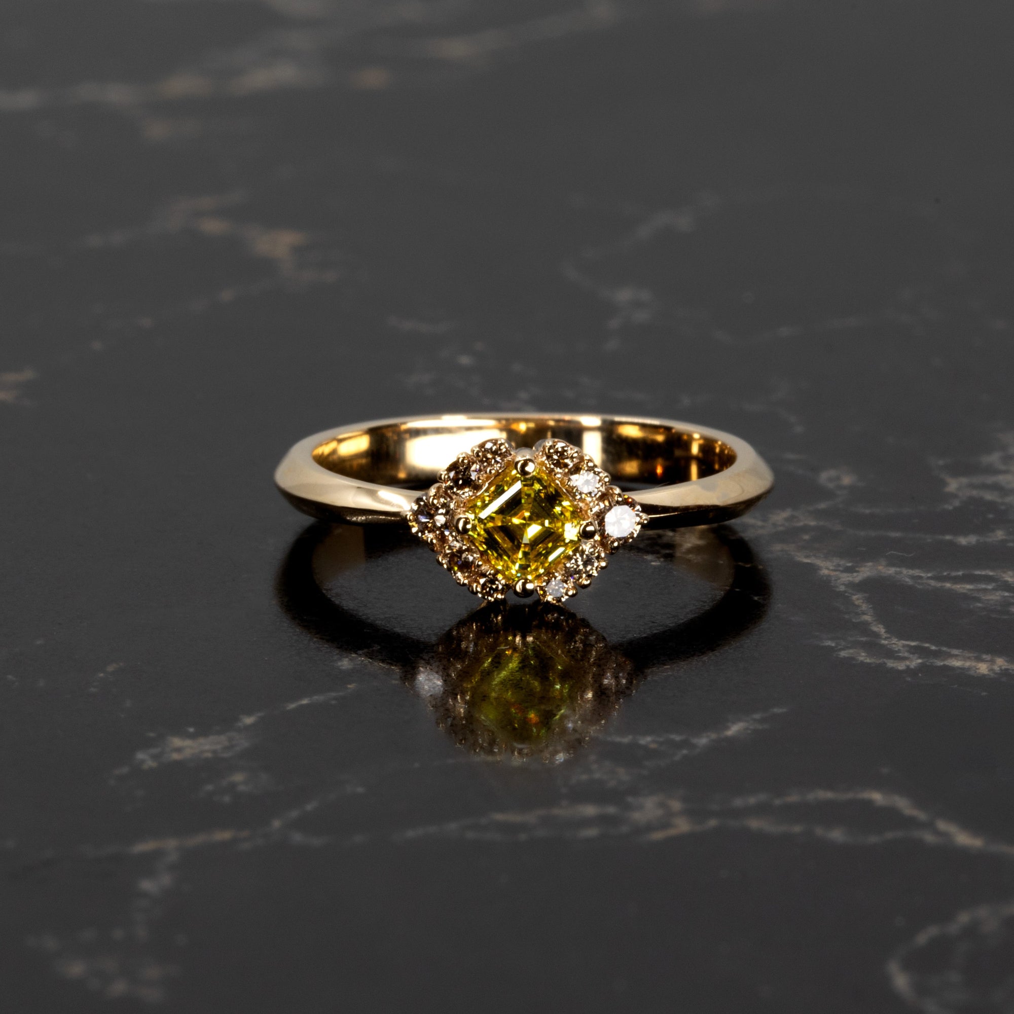 Elegant lighting highlights the structure of this 14k gold ring by Bena Jewelry, crafted in Montreal with a vivid yellow Asscher diamond and brown diamond halo, on a black surface.