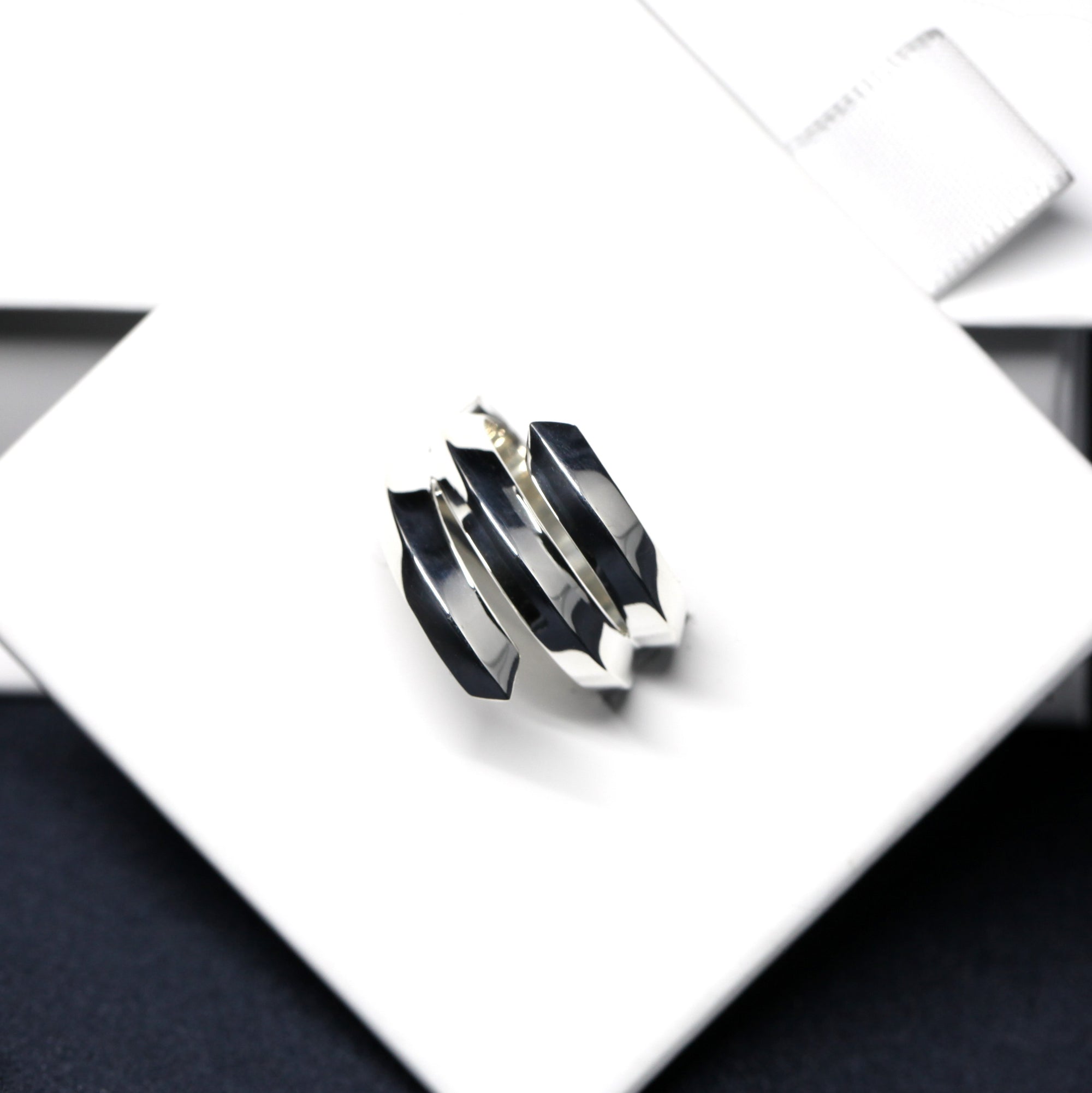 Embrace Ring in White Gold on soft-toned background – The sleek geometric structure of this unisex ring contrasts elegantly with the neutral backdrop.